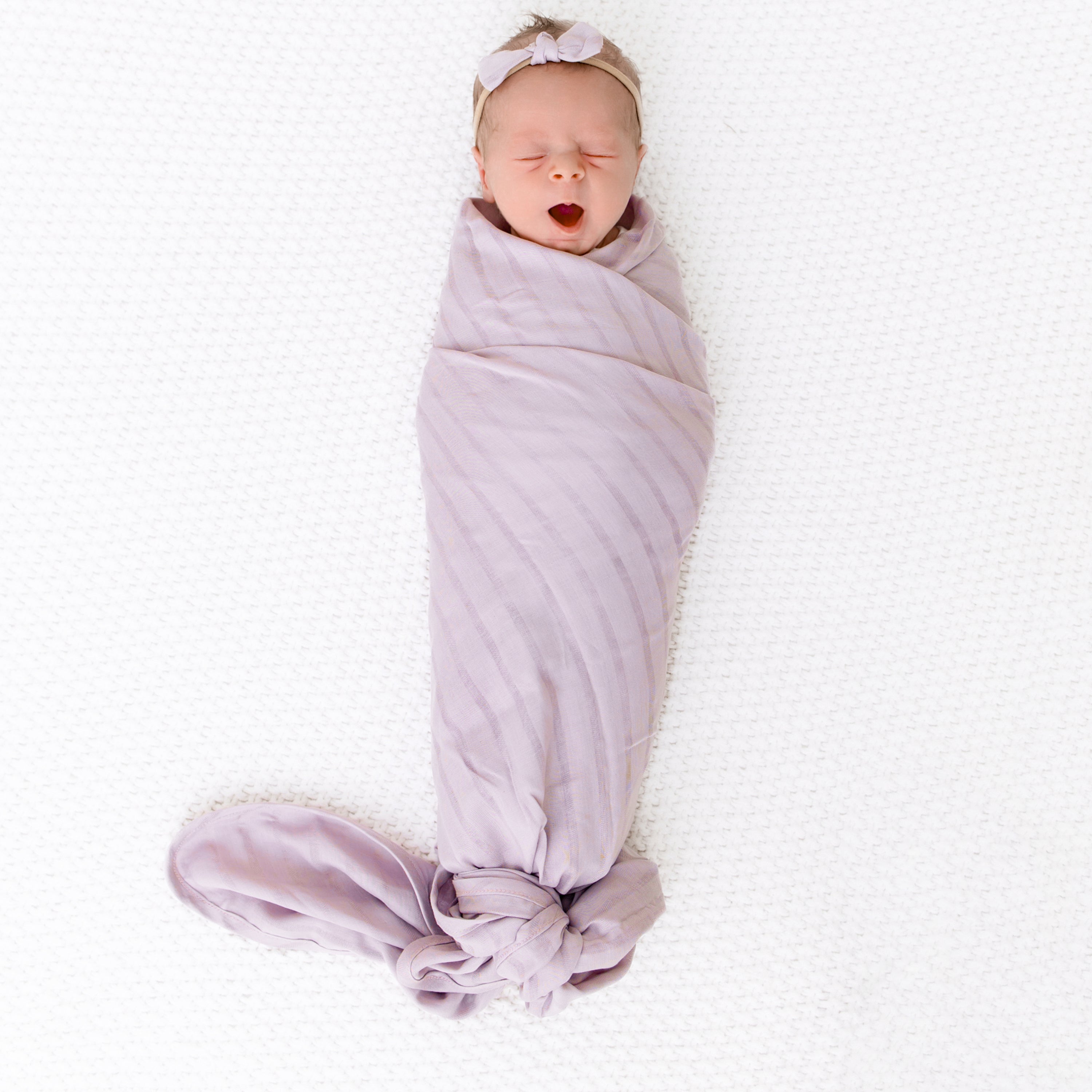 Newborn wrapped in Bamboo Muslin Swaddle Blanket in Wisteria with Matching Purple Bow