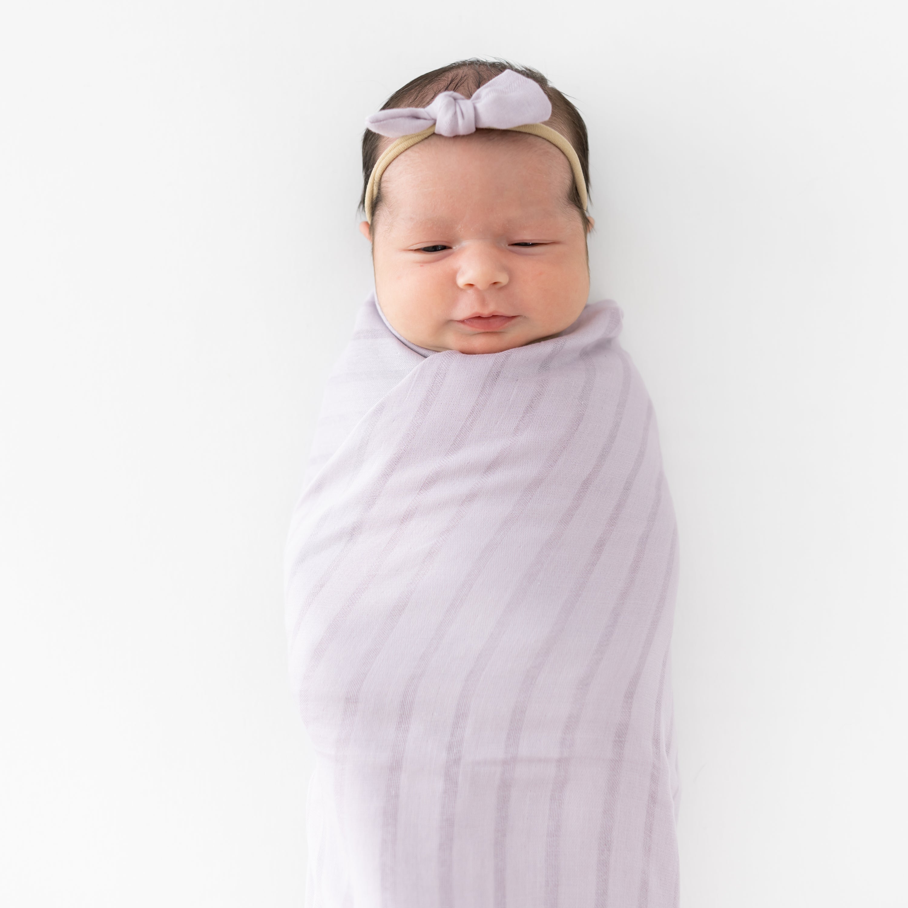 Newborn wrapped in swaddle blanket with matching Bamboo Muslin Tiny Bow in Wisteria