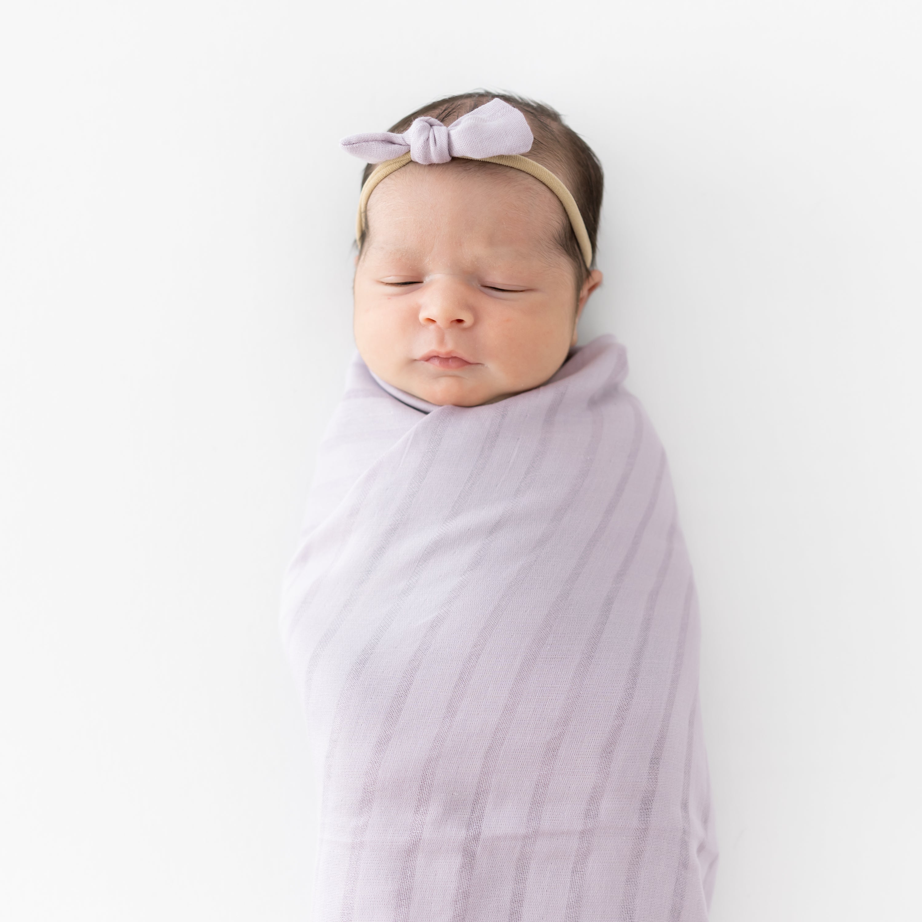 Newborn wearing Bamboo Muslin Tiny Bow in Wisteria with matching purple swaddling blanket