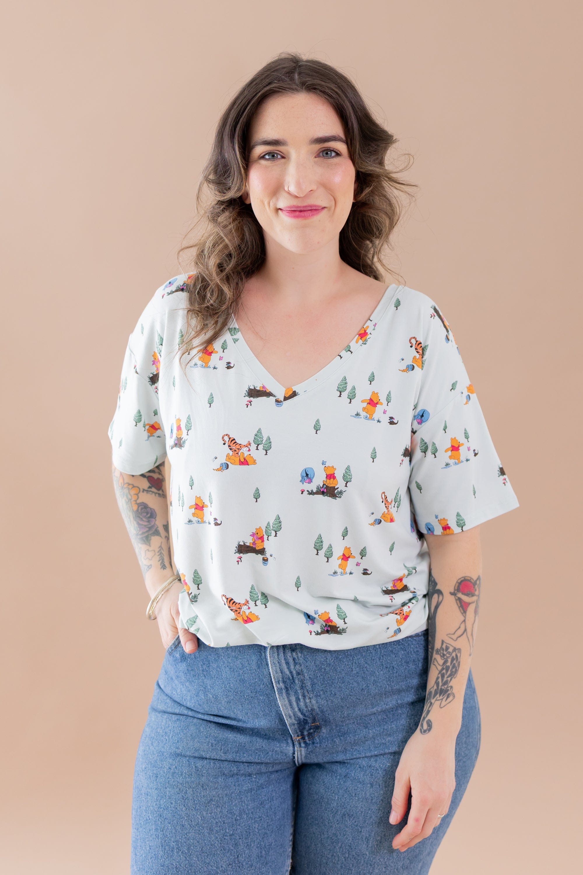 Smiling female modeling the Women's Relaxed Fit V-Neck in Winnie the Pooh Hundred Acre Wood with medium wash jeans