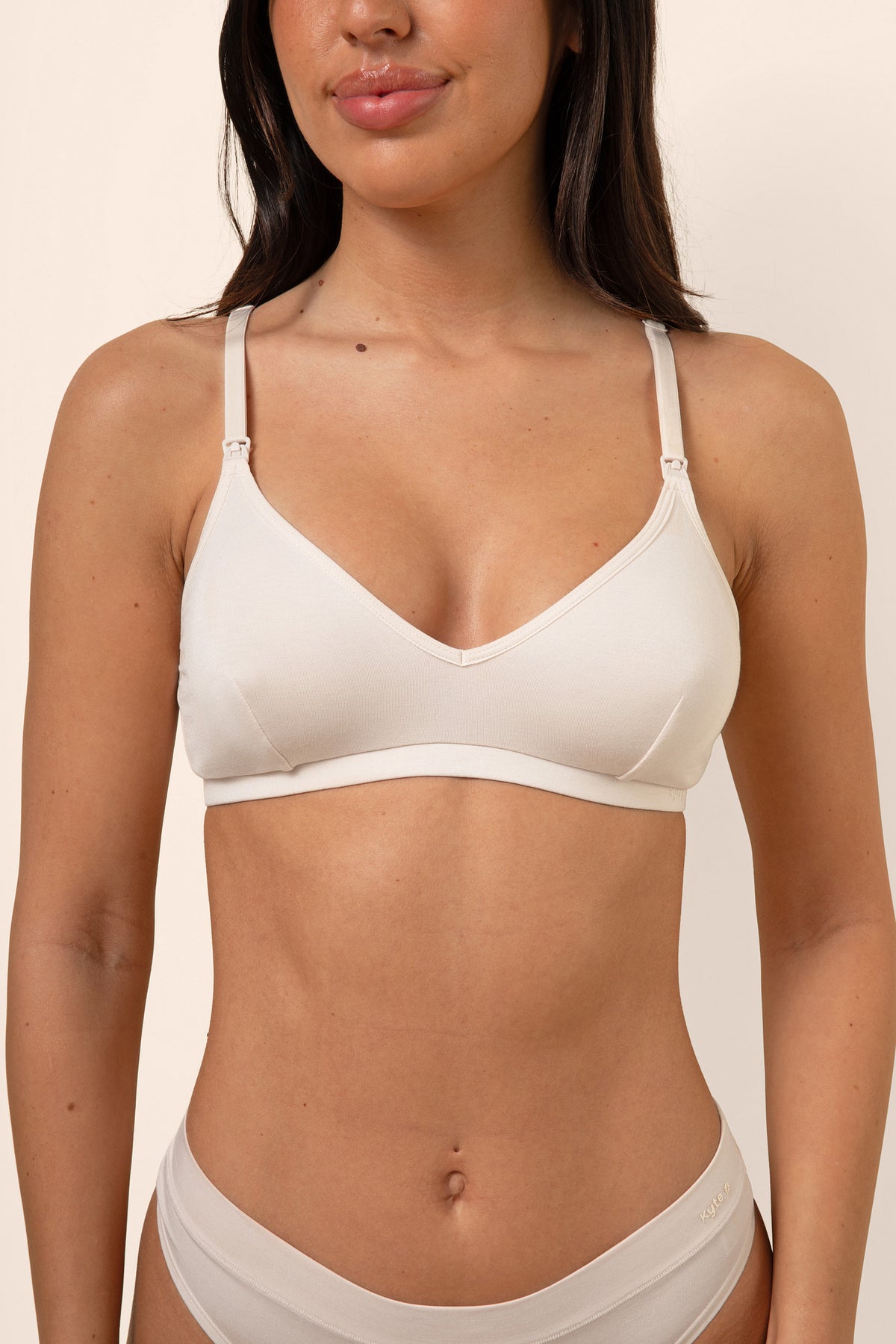 Woman wearing a light beige nursing bra and underwear set against a beige background