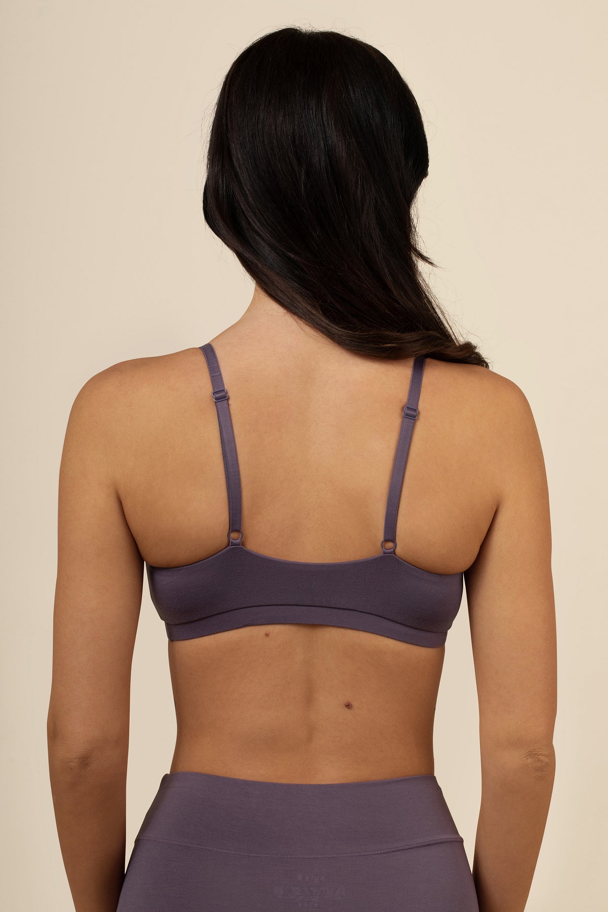 Woman wearing a purple sports bra and leggings on a beige background