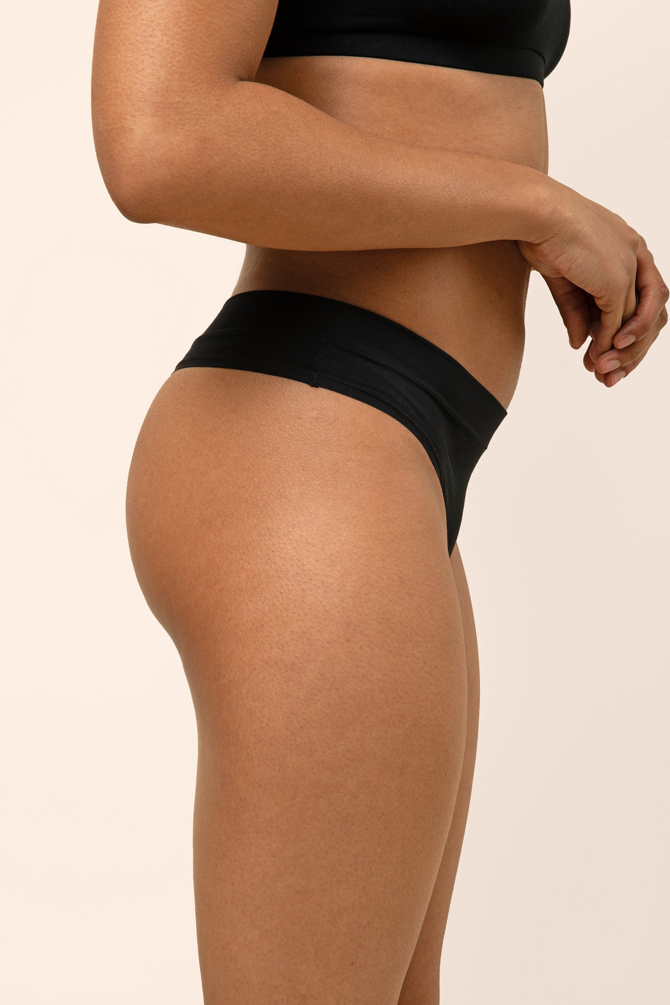 Black thong worn by a woman on a beige background showing side coverage