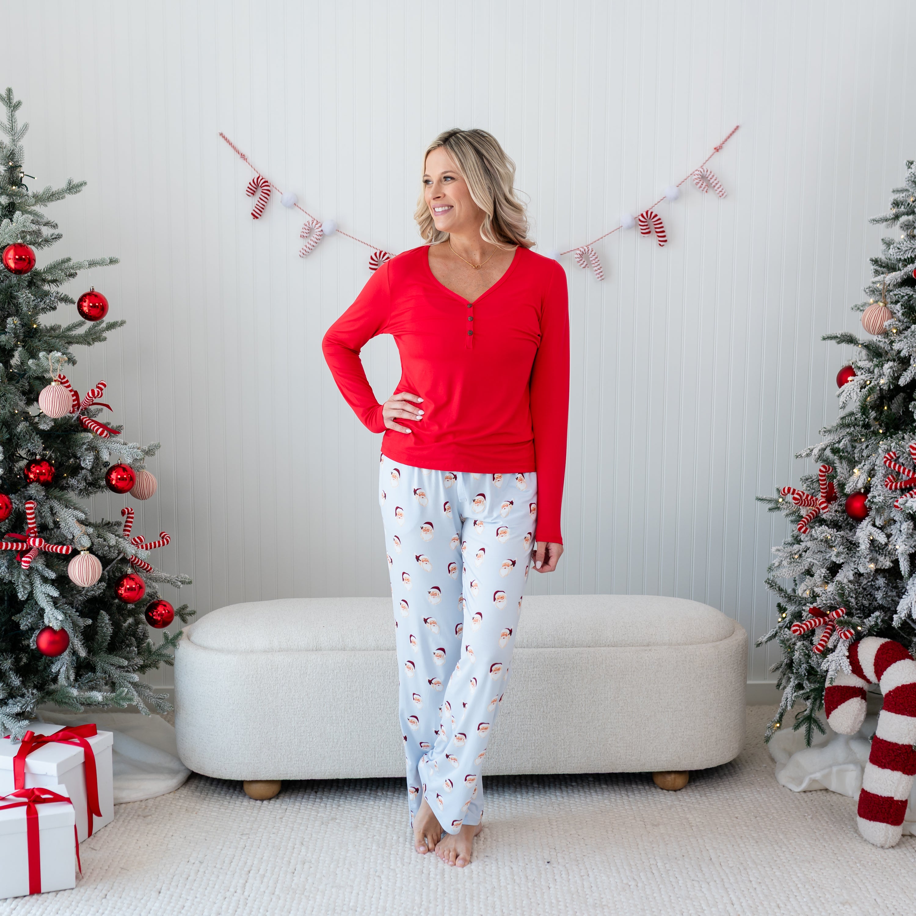 Female model standing in front of a cream colored ottoman wearing the Women's Lounge Pants in Vintage Santa with a cardinal women's henley