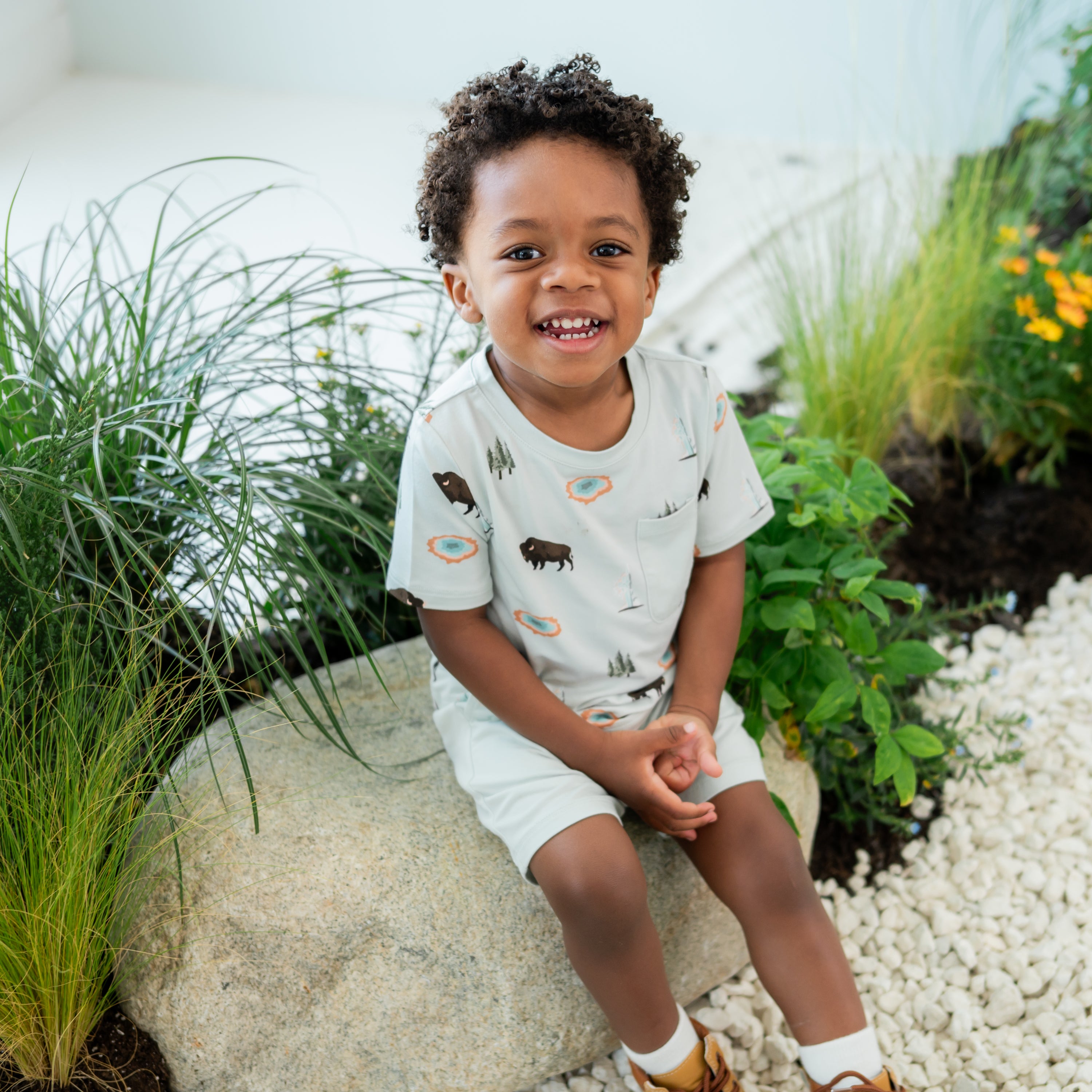 Toddler modeling Toddler Crew Neck Tee in Yellowstone sitting on a stone on nature trail backdrop
