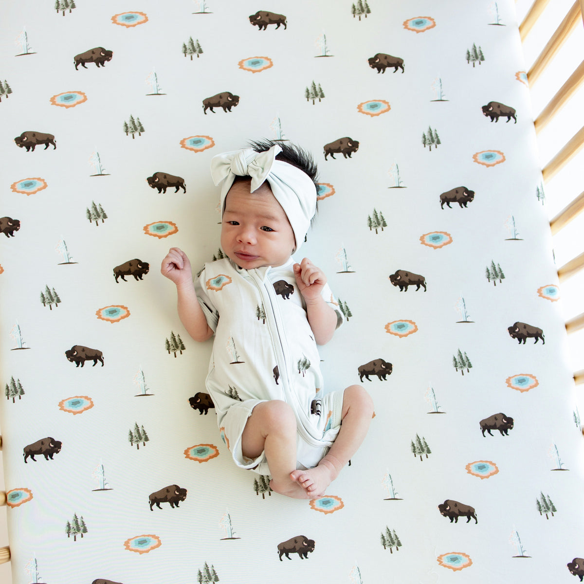 Baby in Zipper Shortall Romper in Yellowstone laying in a crib with Crib Sheet in Yellowstone on