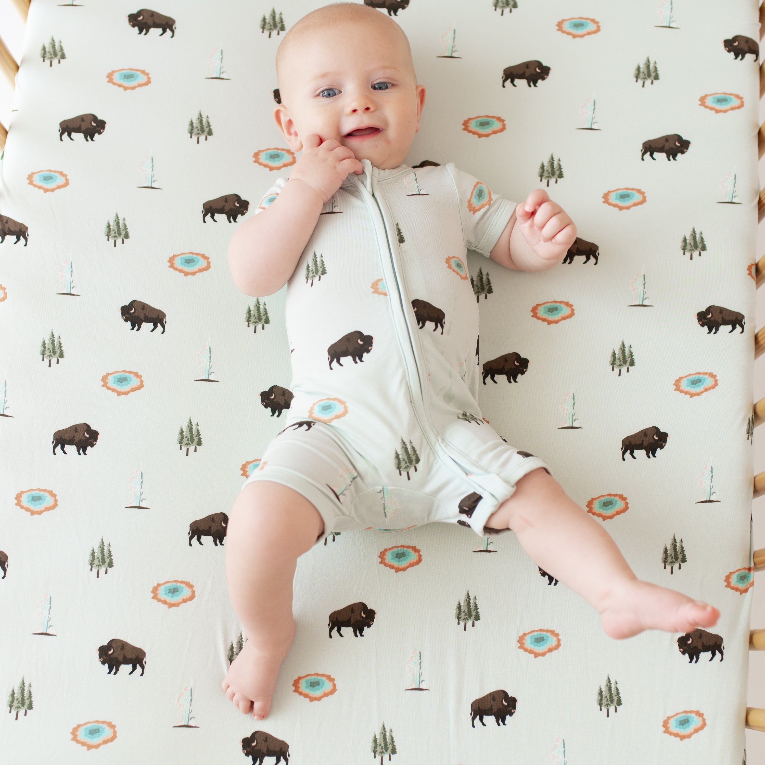 Baby in Zippered Shortall Romper in Yellowstone in crib with Yellowstone crib