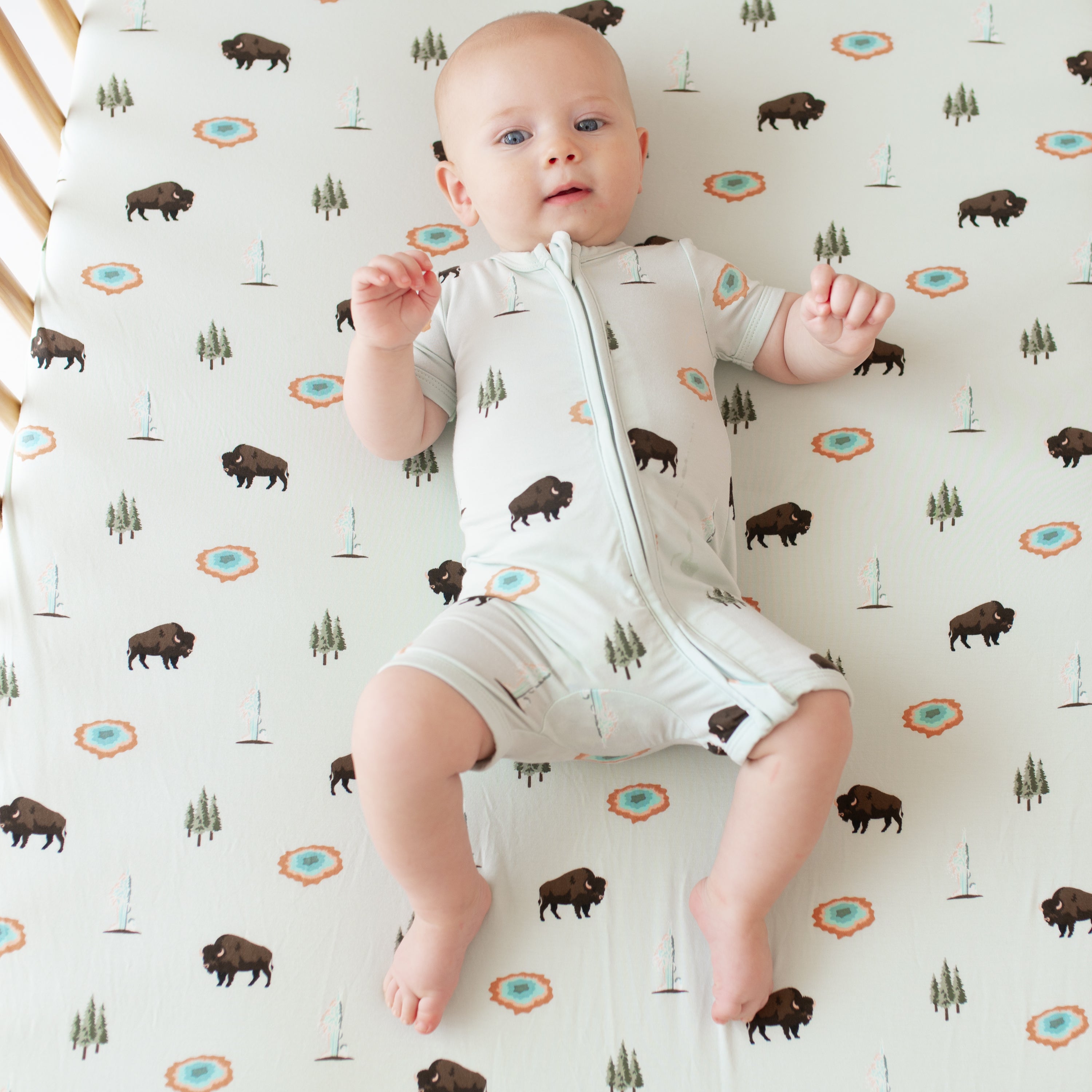 Baby in Zippered Shortall Romper in Yellowstone in crib with Yellowstone crib