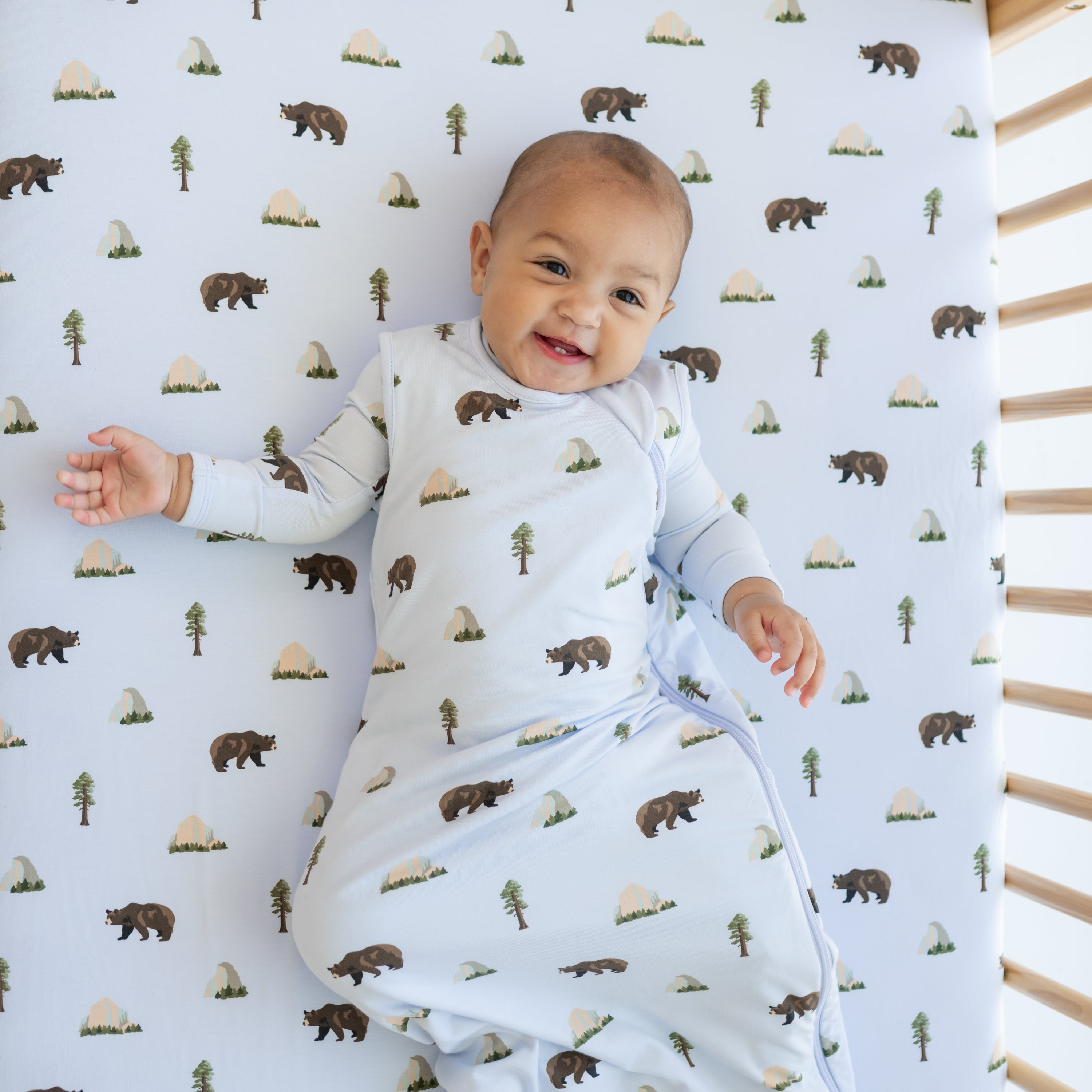 Baby wearing Sleep Bag in Yosemite 0.5 and matching romper underneath in a crib