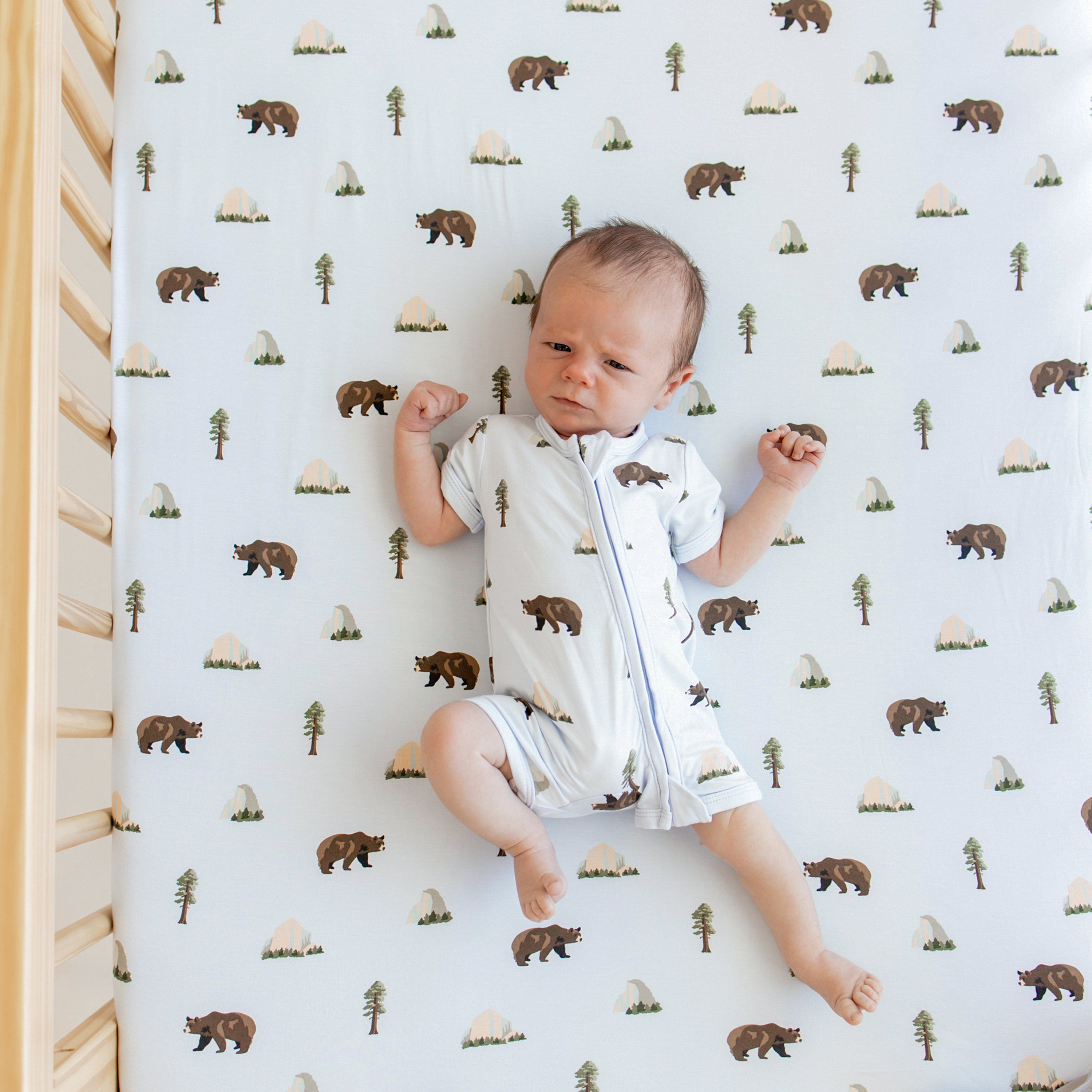 Newborn in Zippered Shortall Romper in Yosemite in crib with matching crib sheet