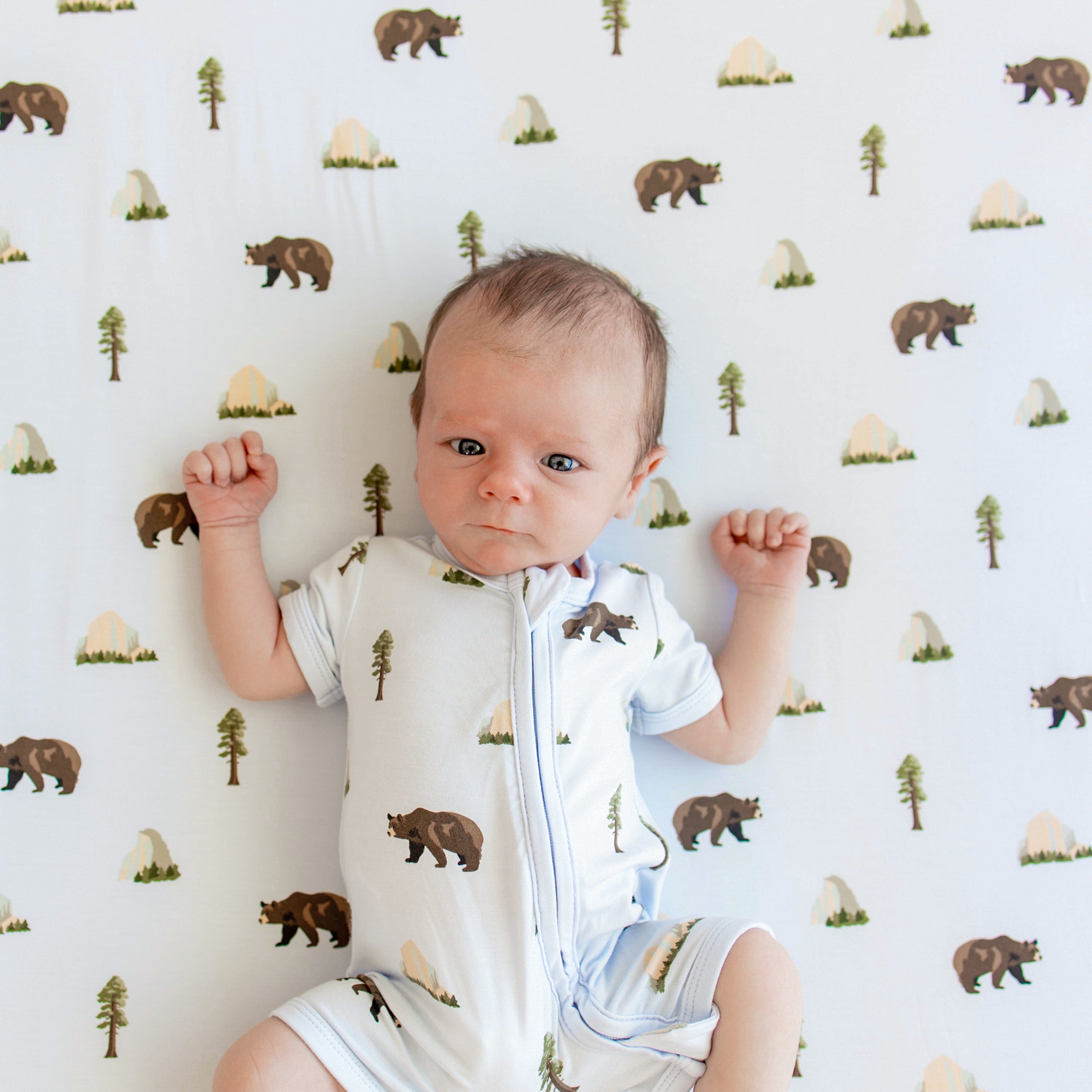 Close up of Newborn in Zippered Shortall Romper in Yosemite in crib with matching crib sheet