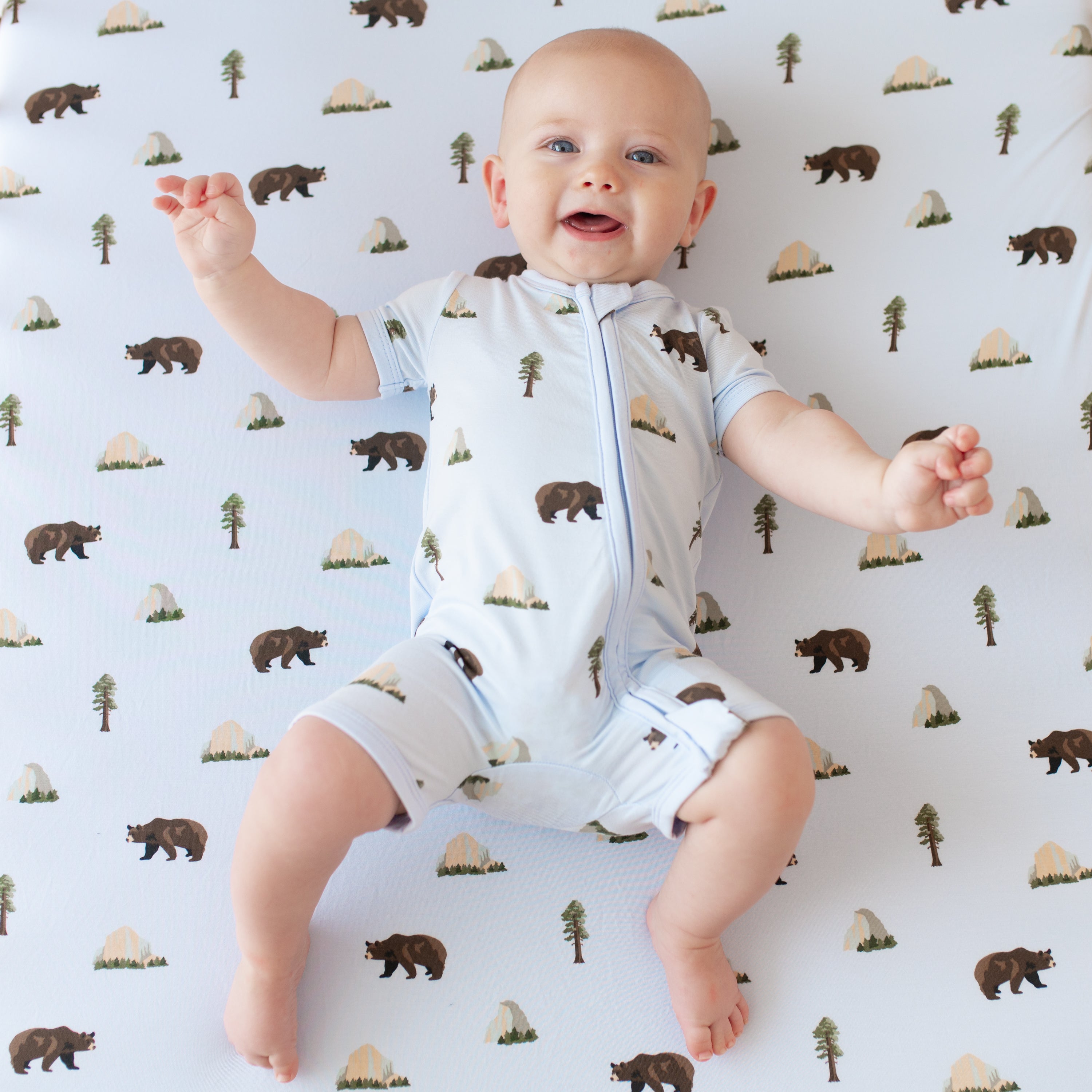 Baby wearing Zippered Shortall Romper in Yosemite on a Yosemite crib sheet