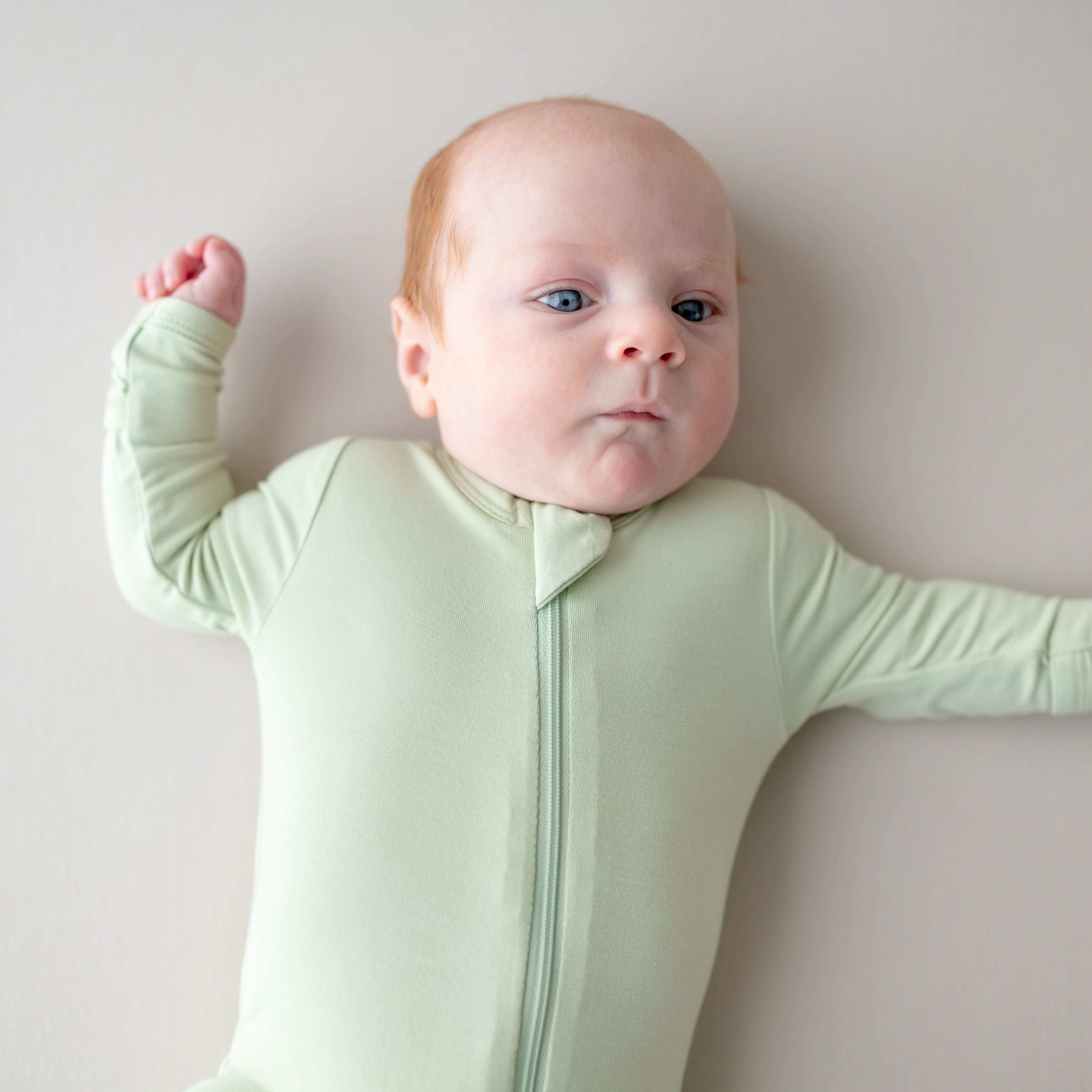 Baby wearing a light green zippered footie on a plain background