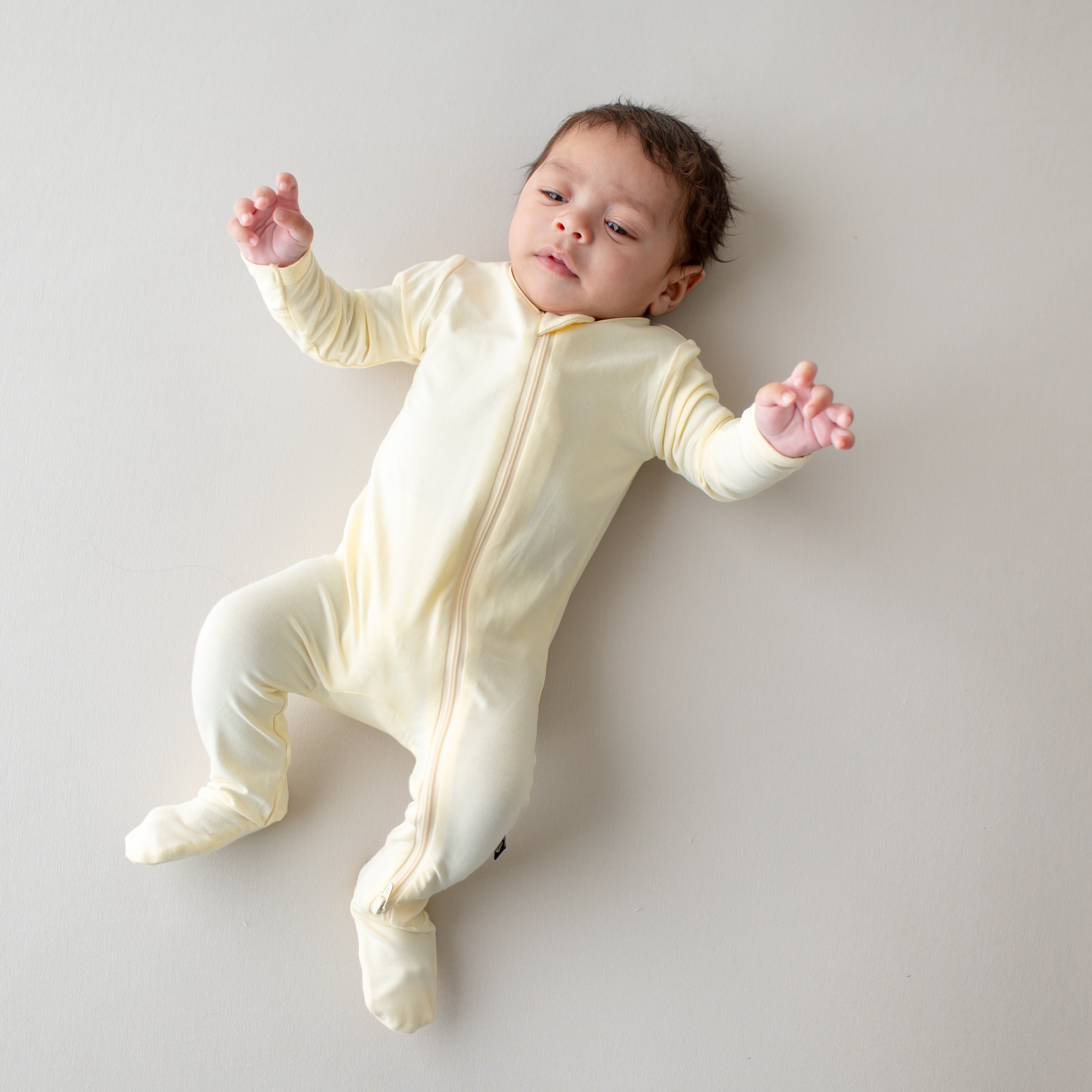 Baby wearing a yellow-colored onesie lying on a light gray surface