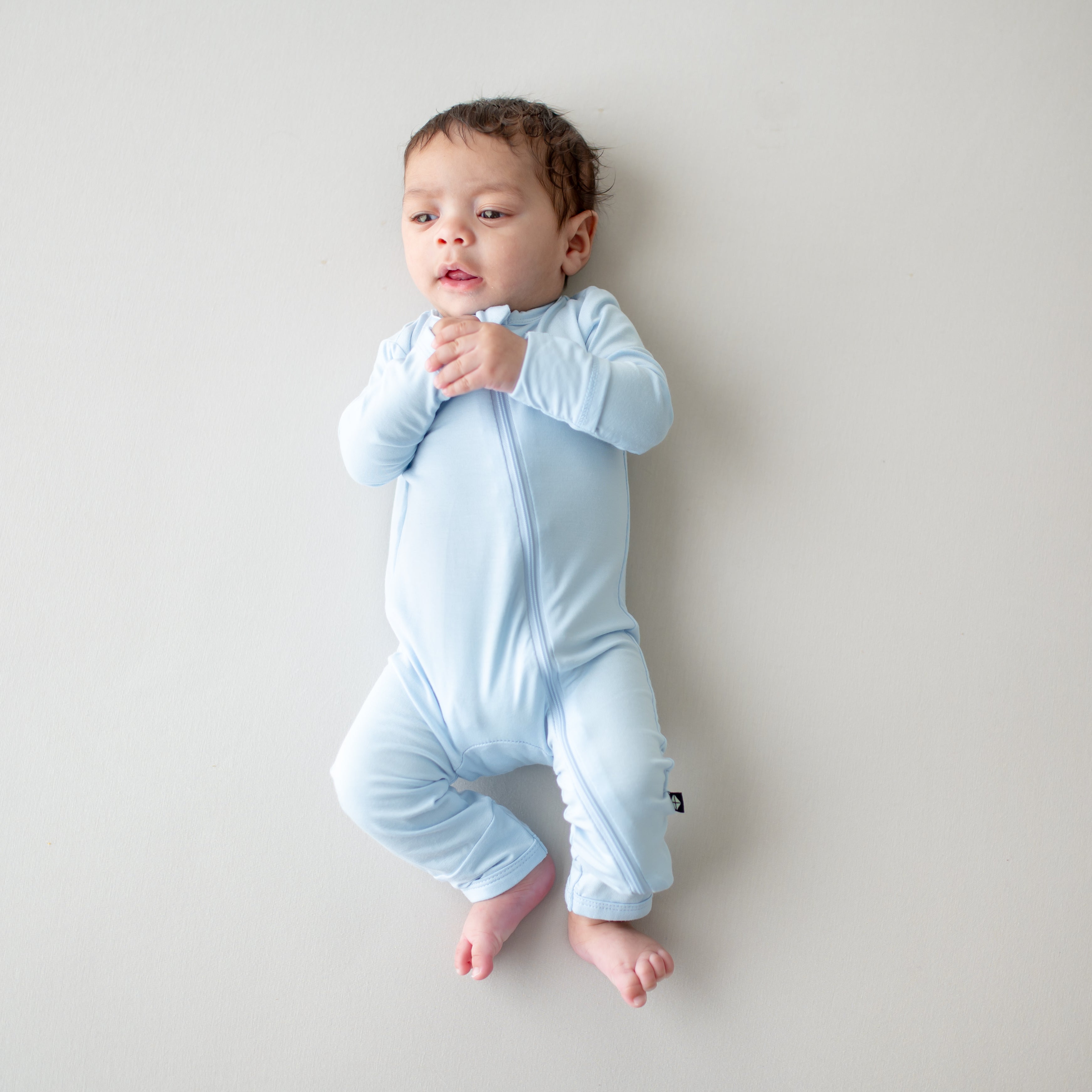 Baby wearing a light blue zippered romper on a plain background
