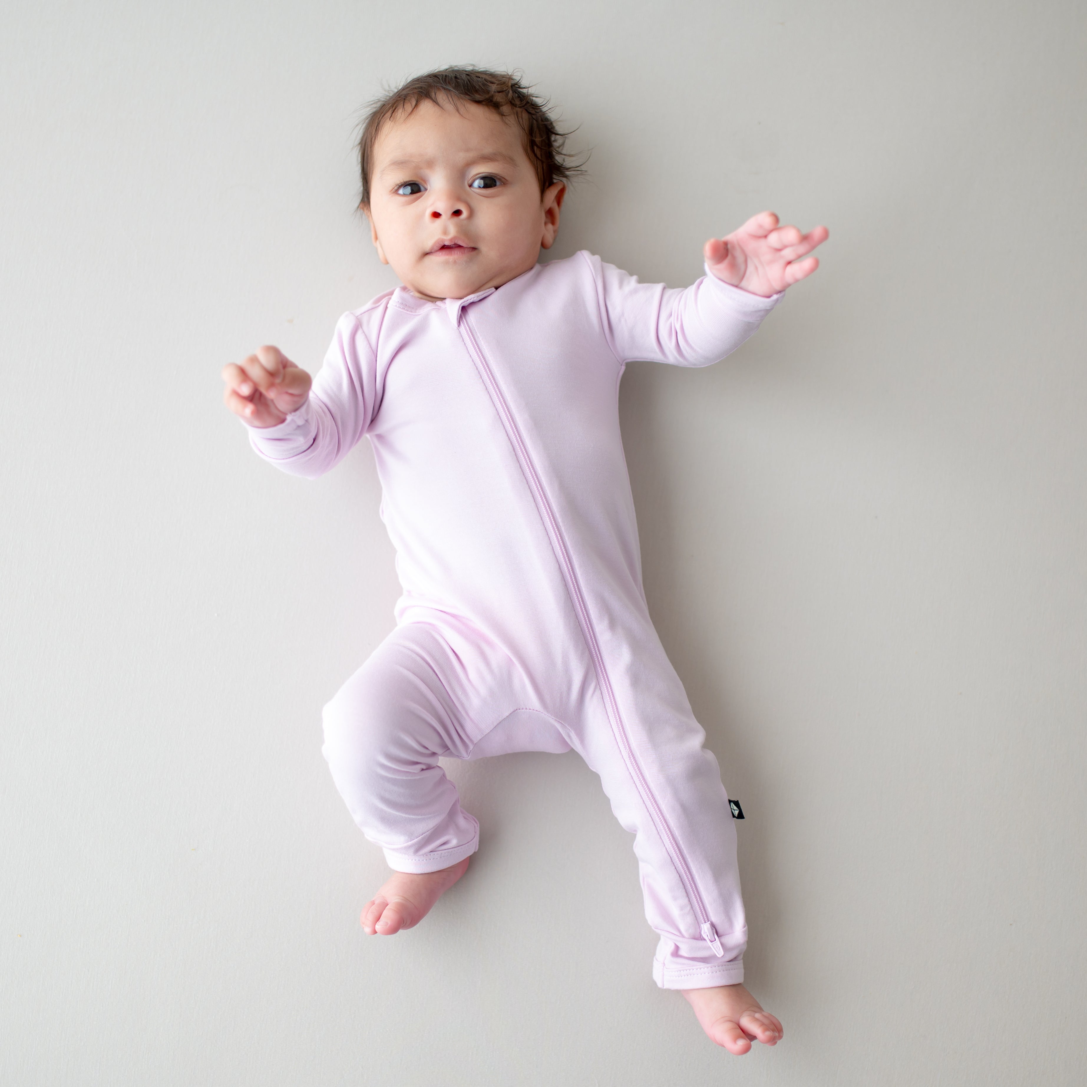 Baby in a light purple romper with zipper laying on a plain background