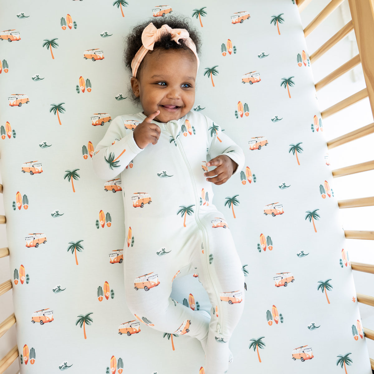 Baby modeling a Dew Surf Zippered Footie while laying in a crib with Crib Sheet in Dew Surf on