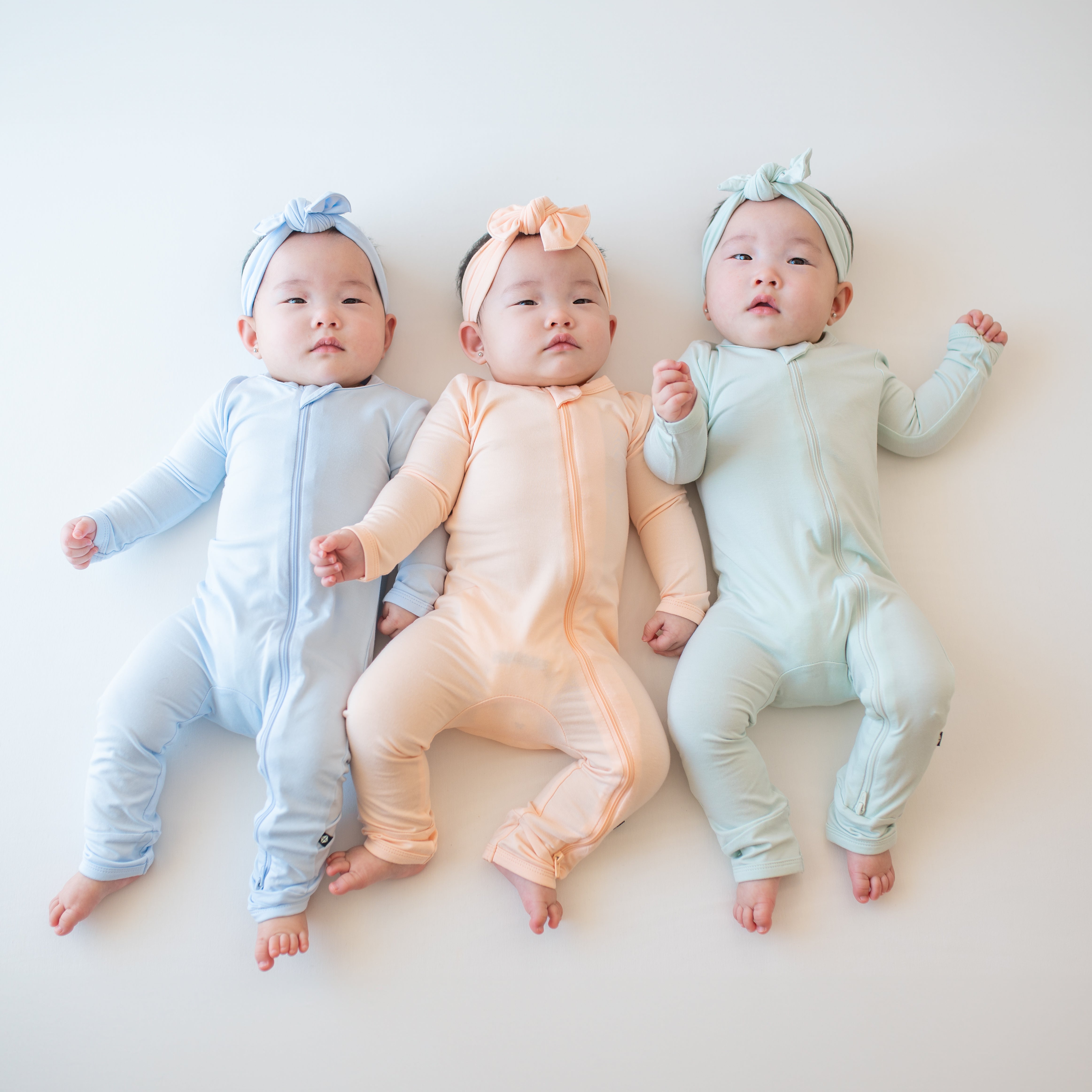 Three infant girls wearing the Zippered Rompers in the Summer Solid colors with matching knotted bows