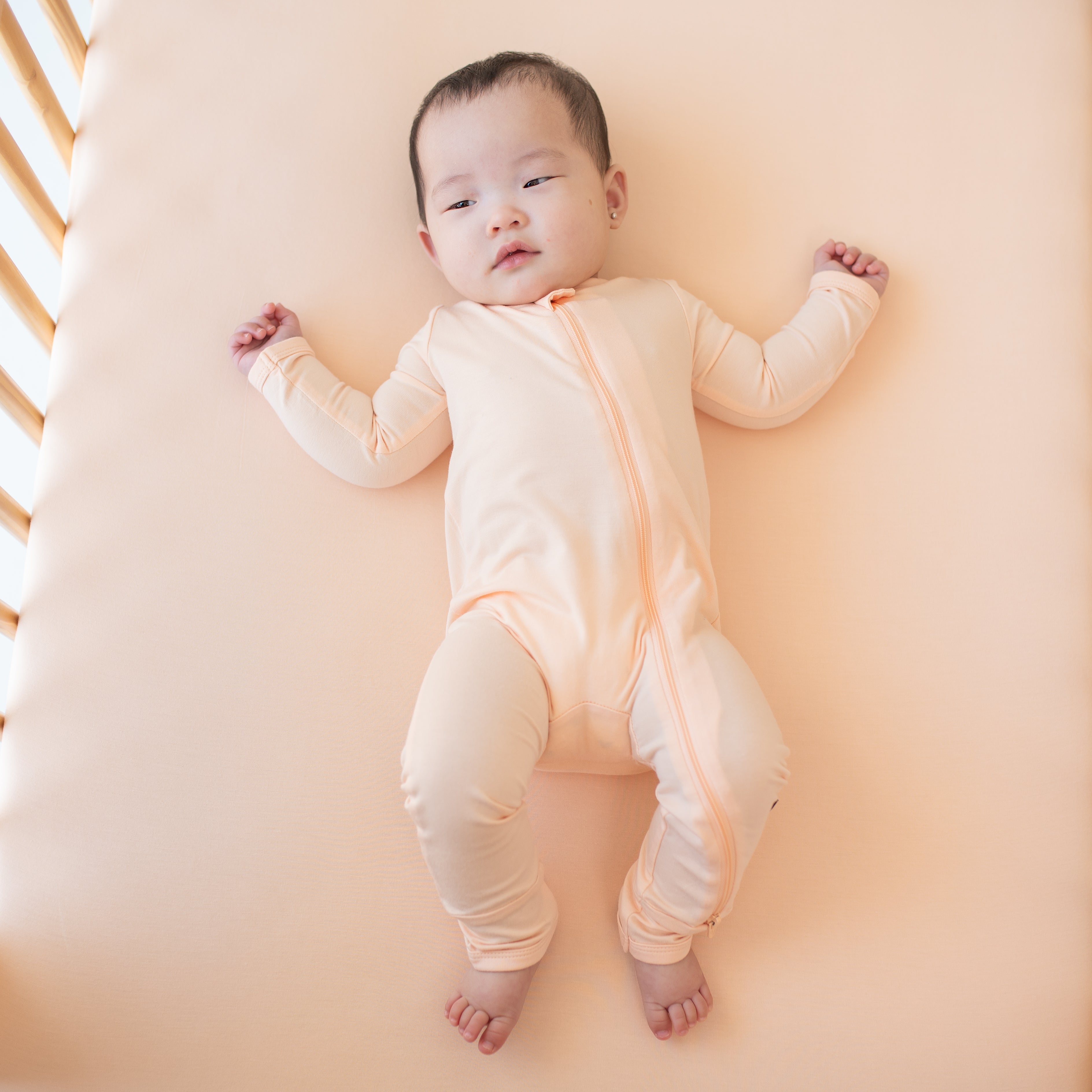 Infant model laying in a crib on a Canyon crib sheet wearing the Zippered Romper in Canyon