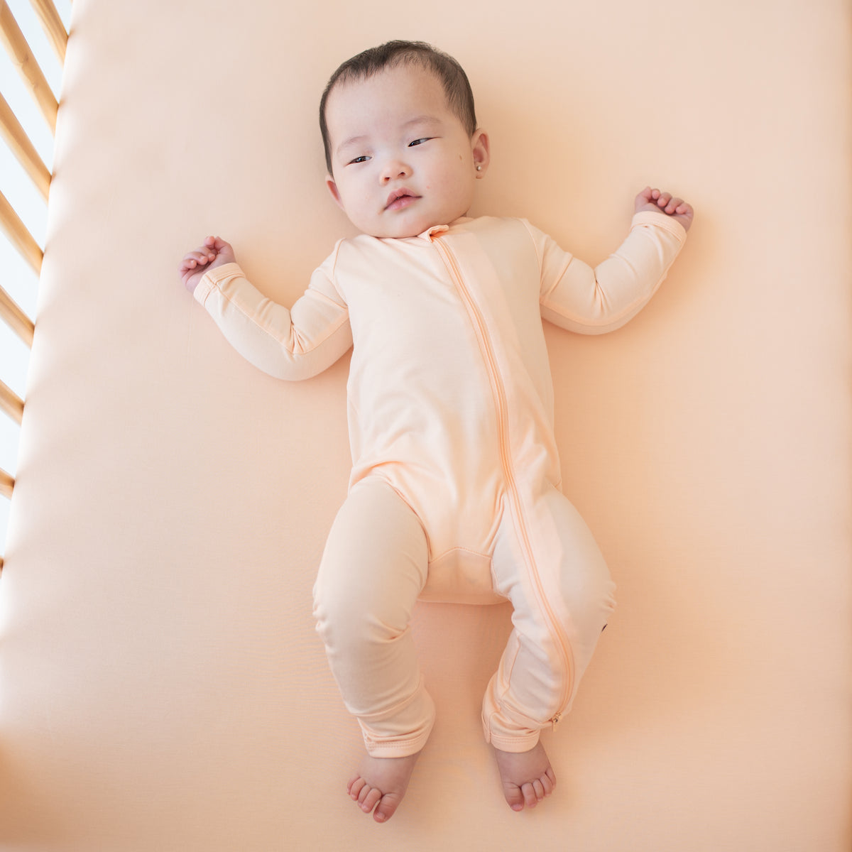 Infant model laying in a crib on a Canyon crib sheet wearing the Zippered Romper in Canyon