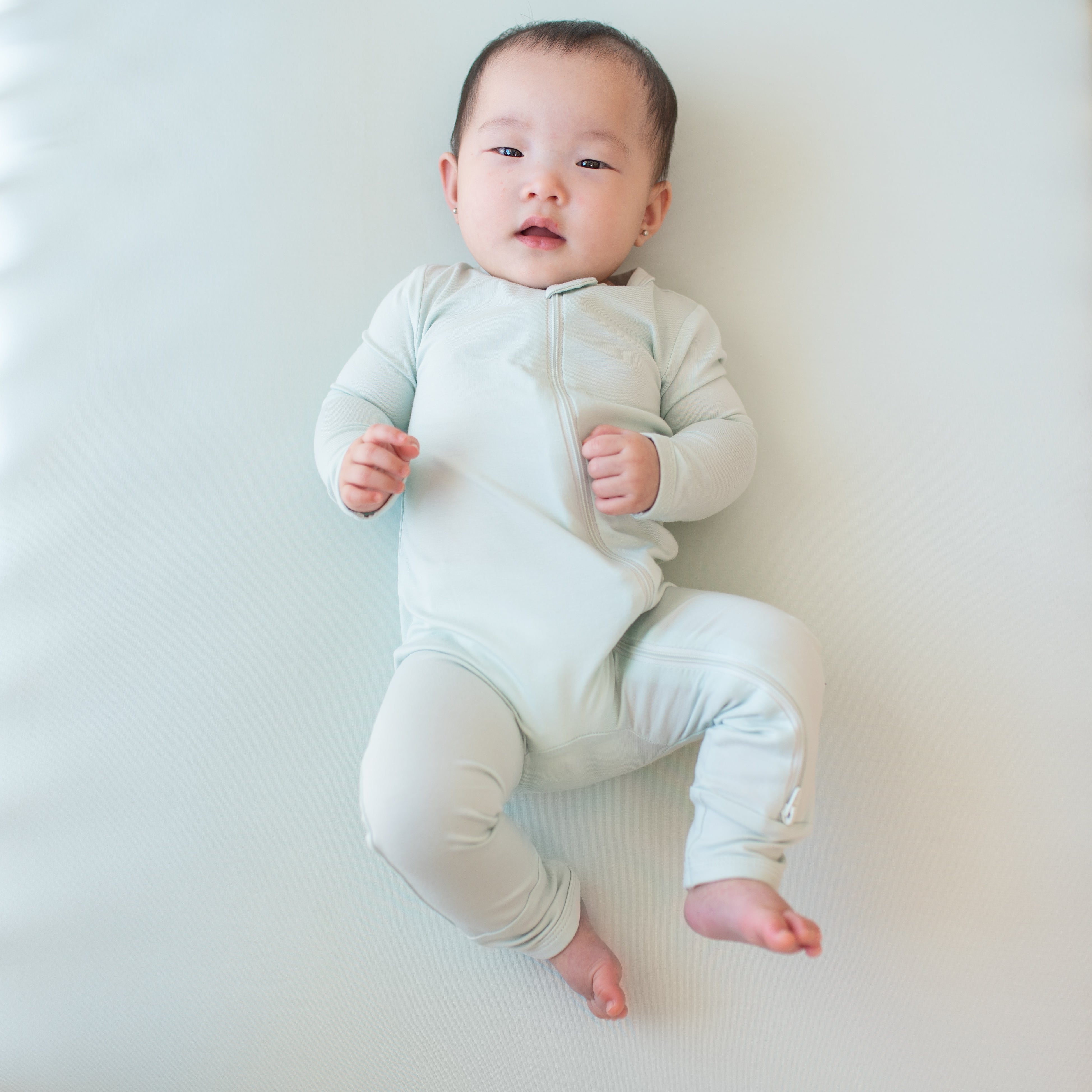 Infant laying down on a Dew blanket wearing the Zippered Romper in Dew