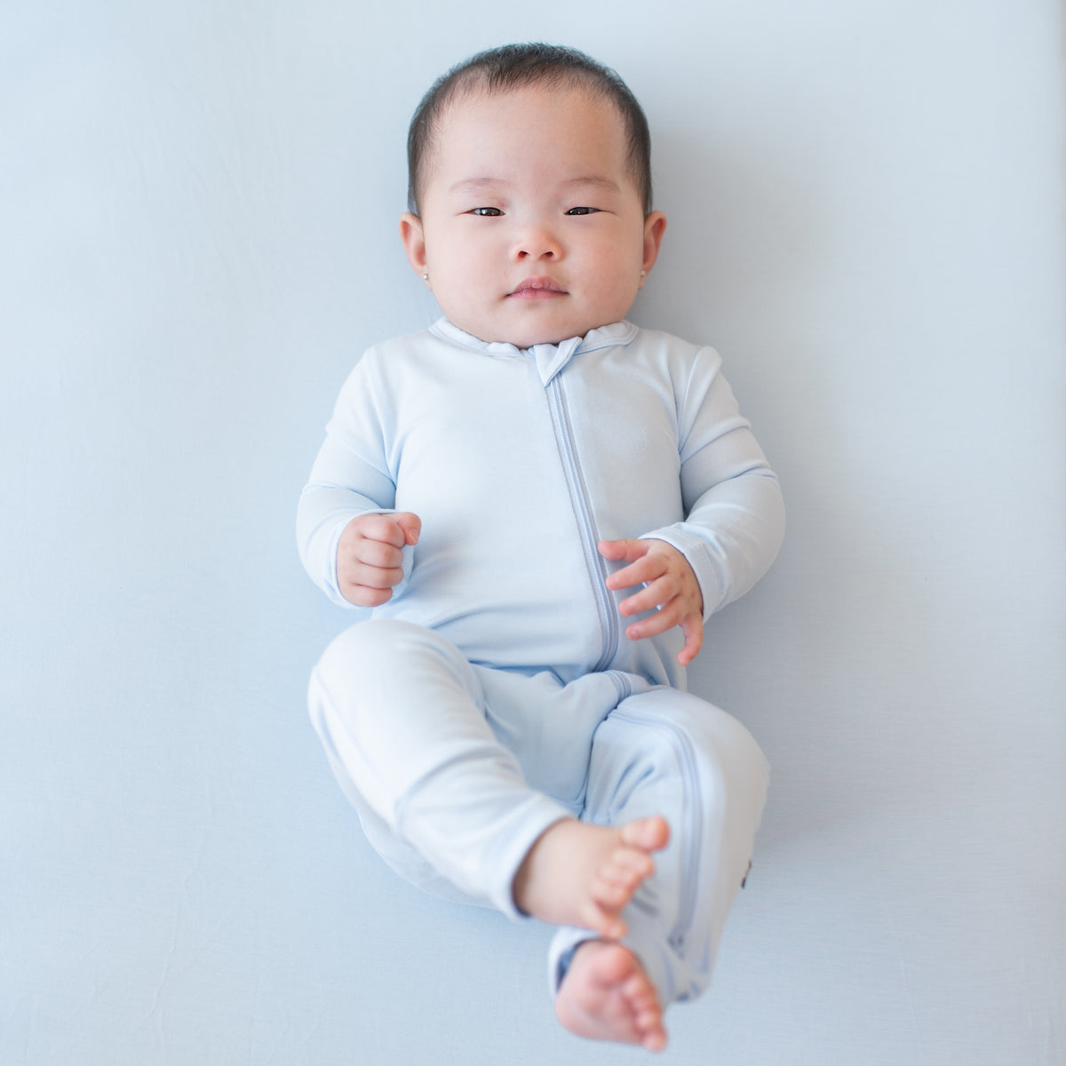 Infant wearing the Zippered Romper in Mist laying on a Mist blanket
