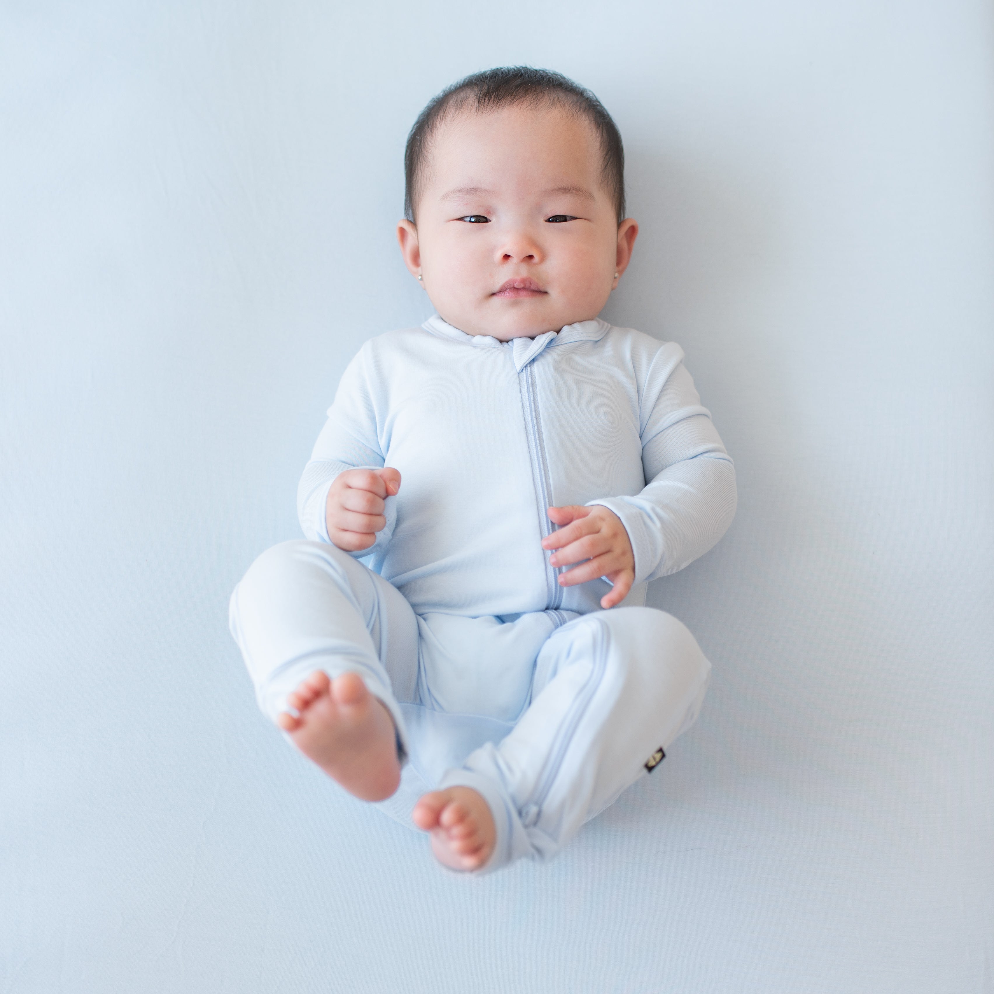 Infant laying on a Mist Blanket wearing the Zippered Romper in Mist