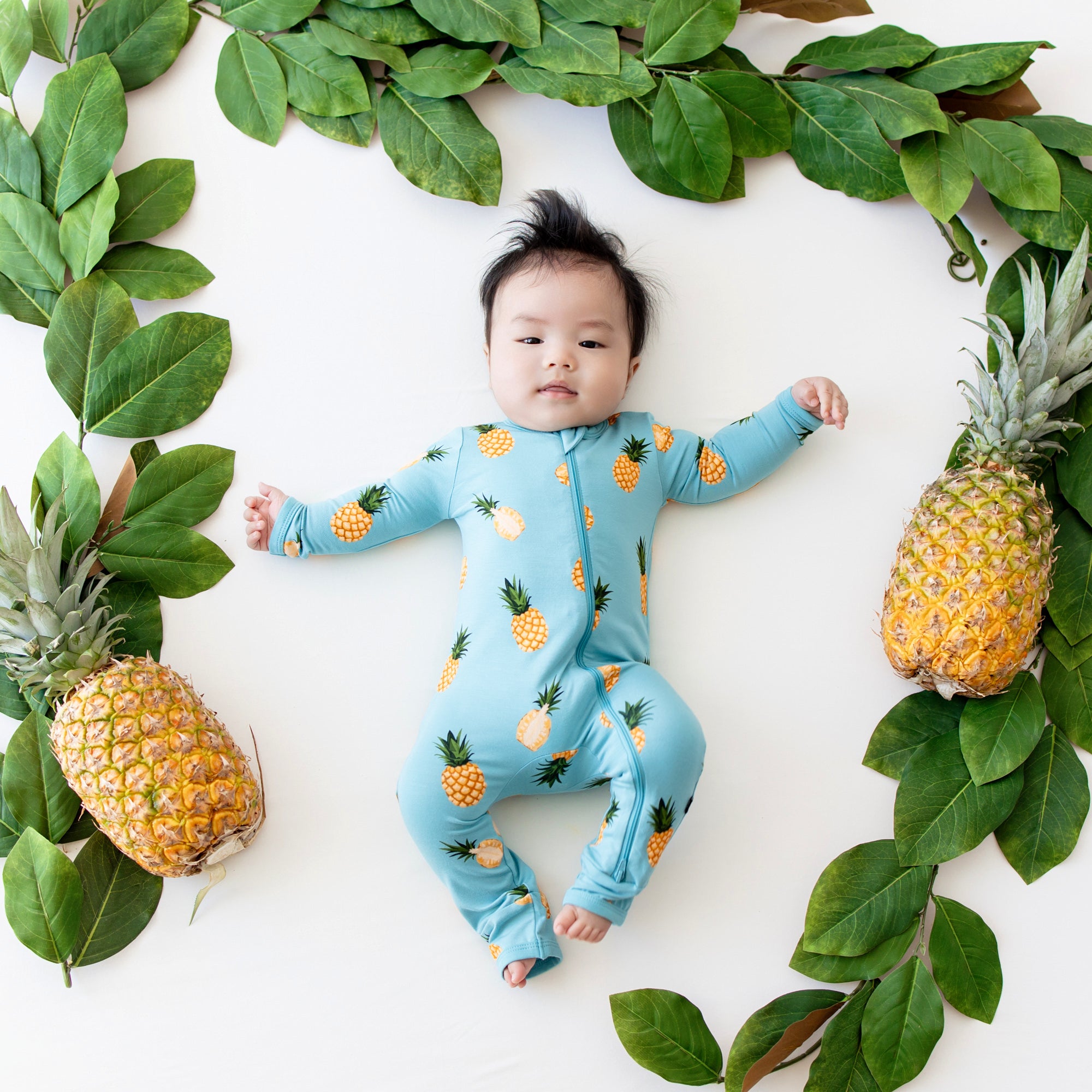 Baby in Zippered Romper in Pineapple surrounded by pineapple and leaves