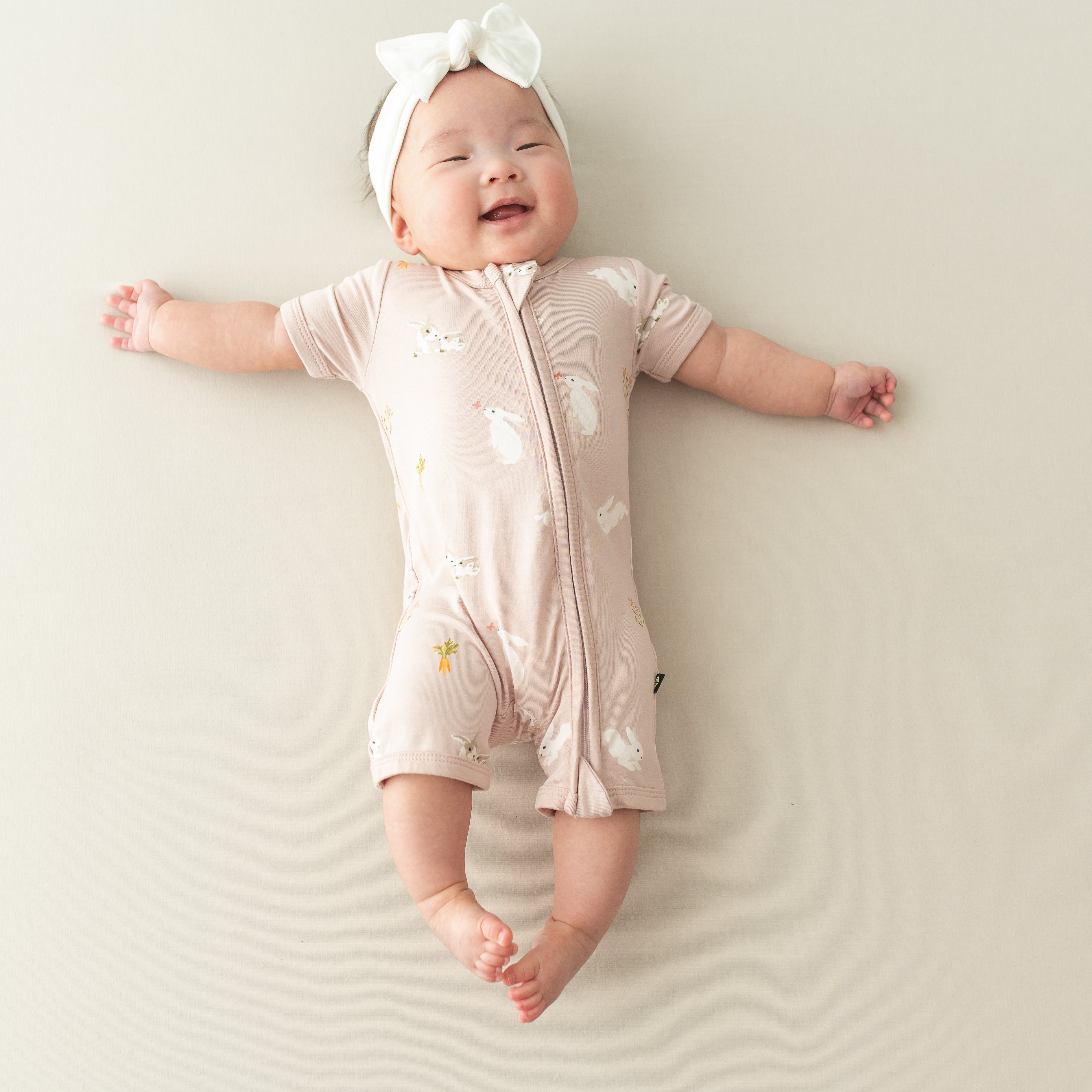 Infant wearing Kyte Baby Zippered Shortall Romper with dual zipper in Blush Rabbit