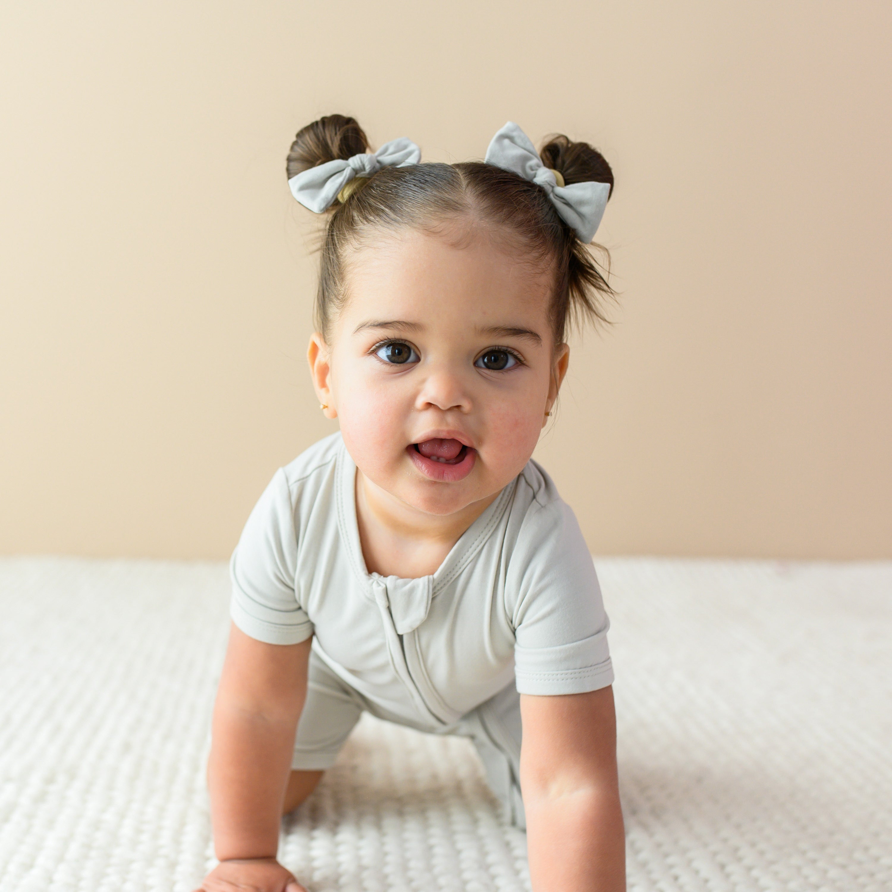 Toddler crawling towards camera while wearing Kyte Baby Zippered Shortall Romper in Oat