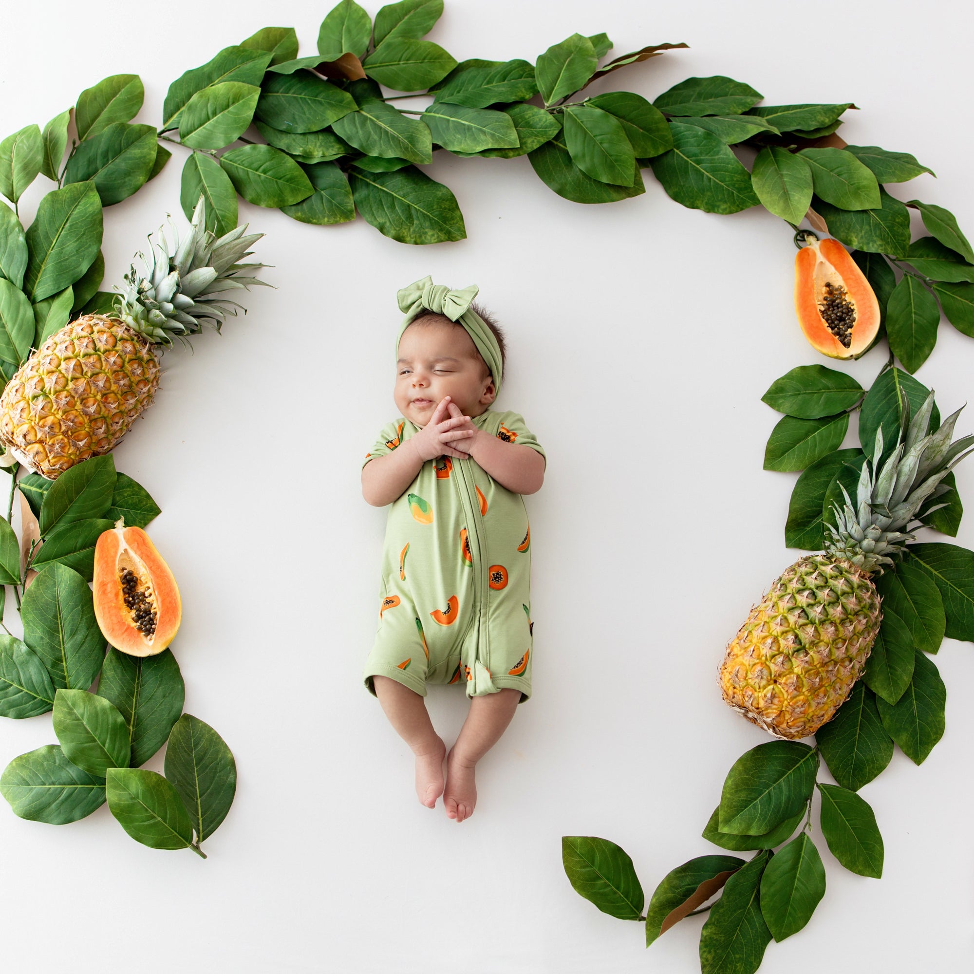 Newborn wearing Kyte Baby Zippered Shortall Romper with dual zipper in Papaya print