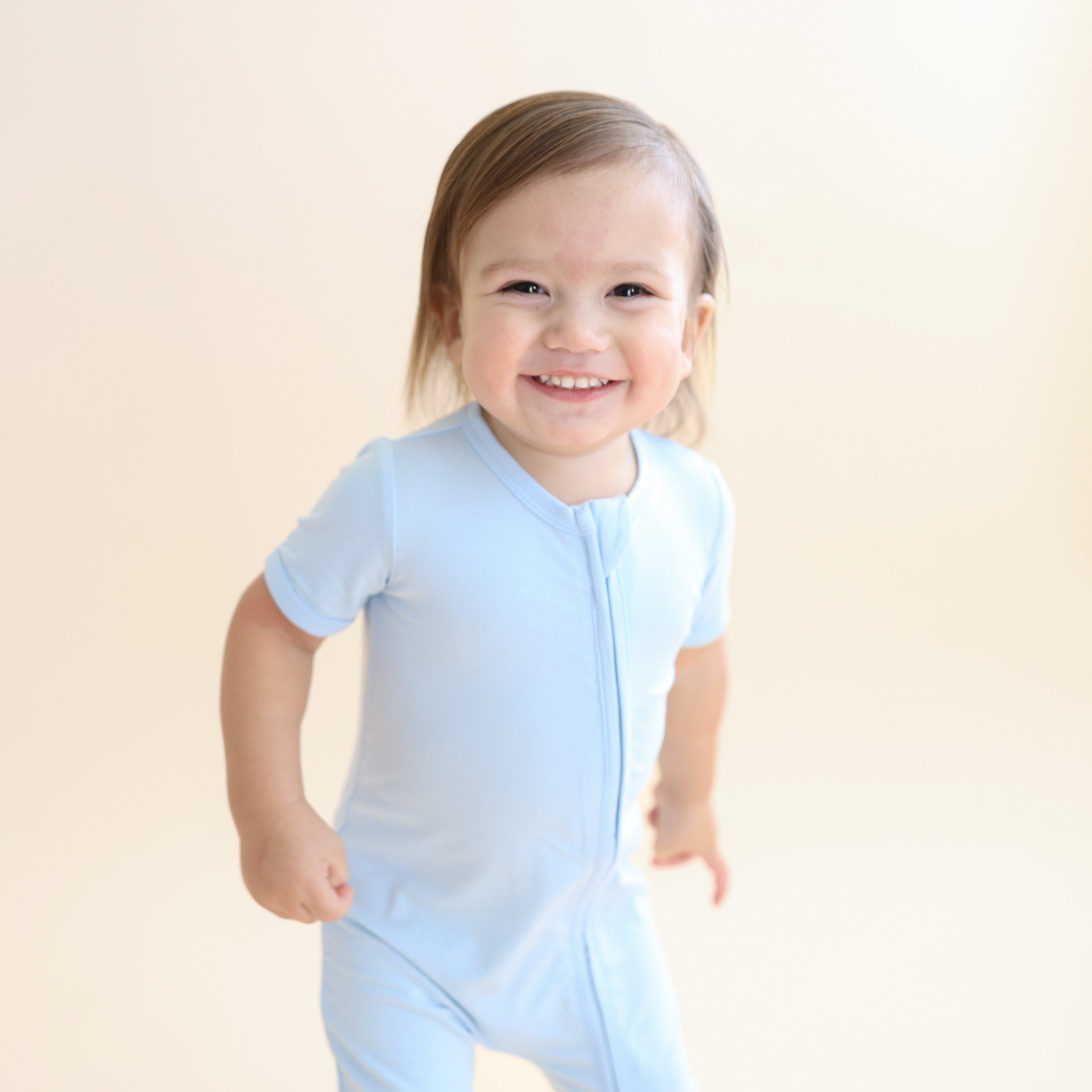 Young smiling boy wearing the Zipper Shortall Romper in Breeze
