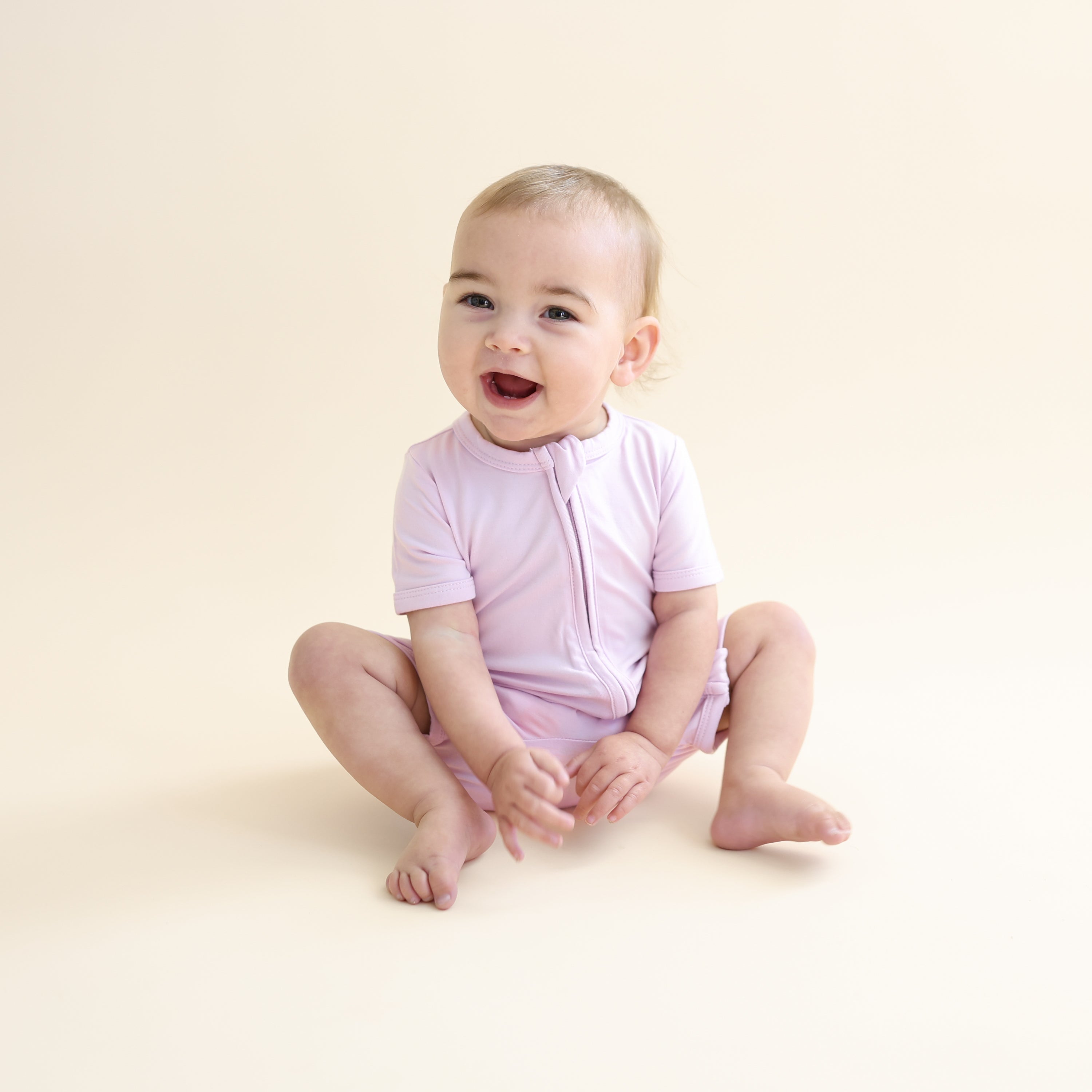 Young toddler sitting on the floor wearing the Zipper Shortall Romper in Thistle
