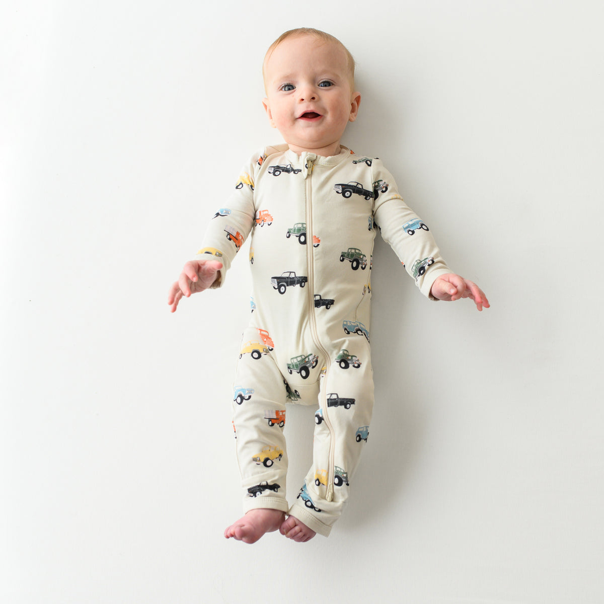 Smiling baby laying down wearing the Zippered Romper in Vintage Truck