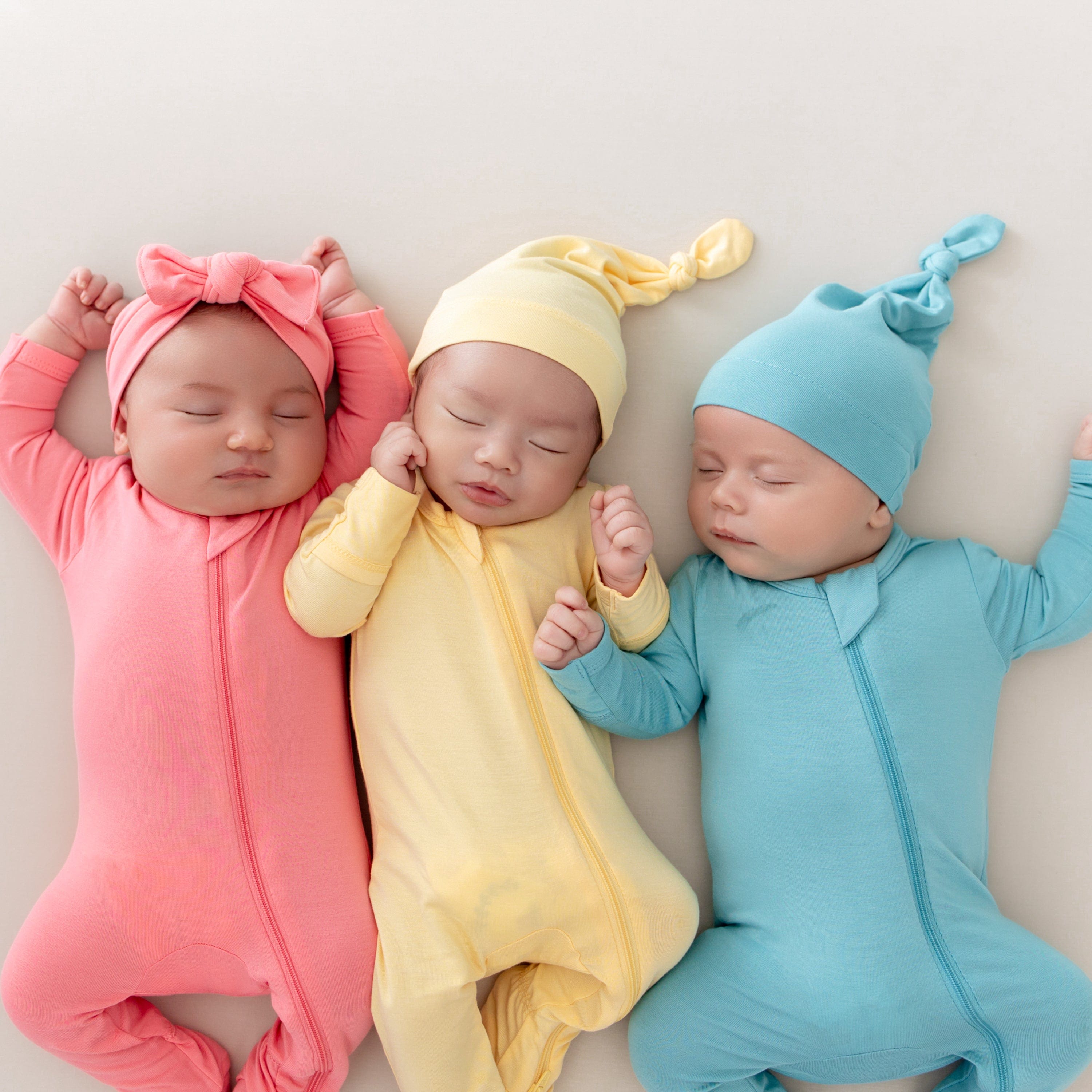 Babies wearing zippered footie pajamas in pink, yellow, and blue