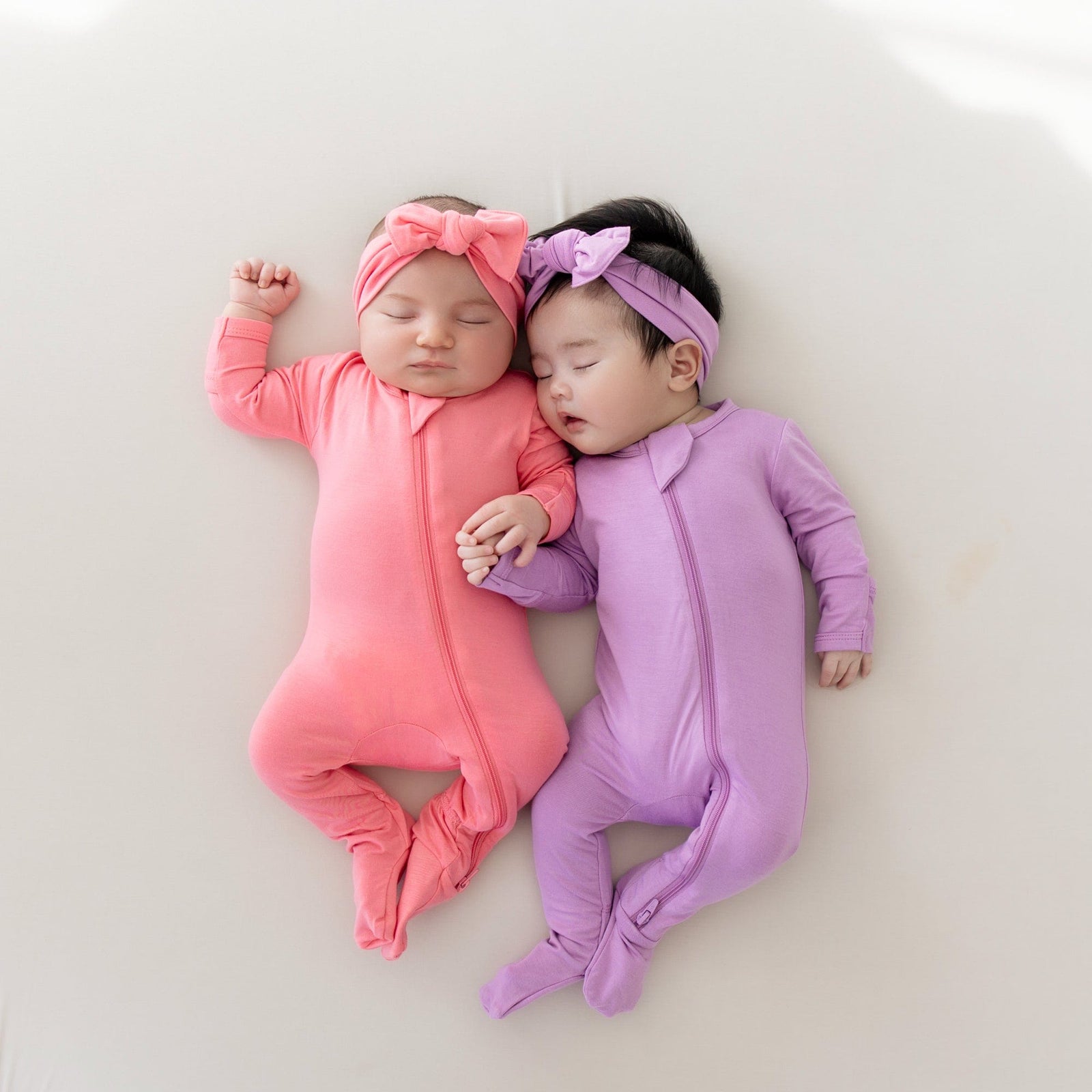 Babies sleeping in zippered footies in guava and poi with matching bows