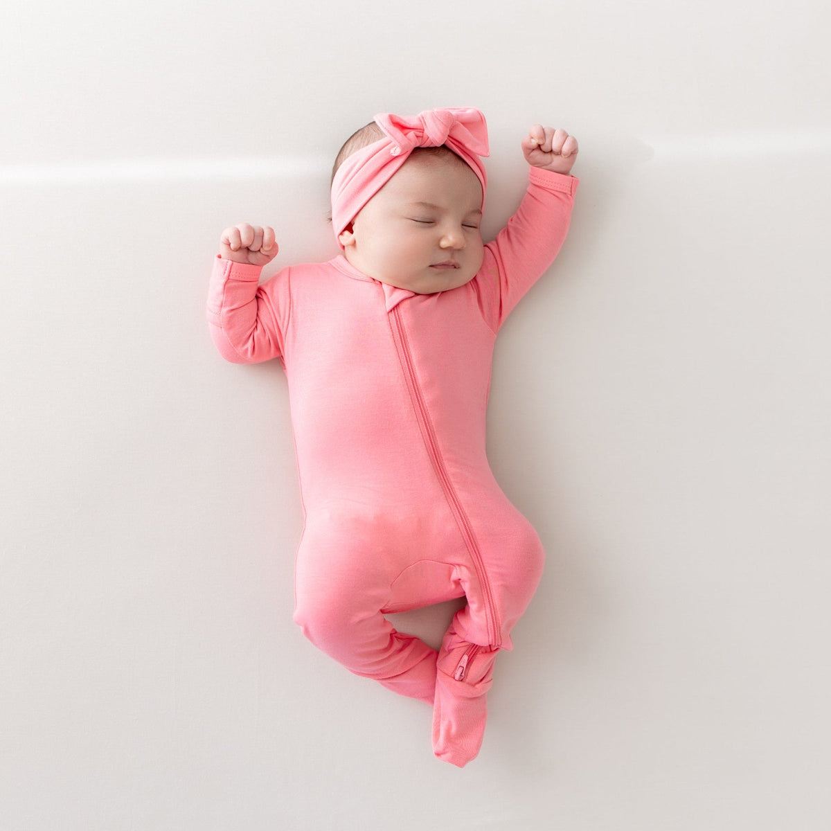 Baby sleeping in zippered footie and bow in guava