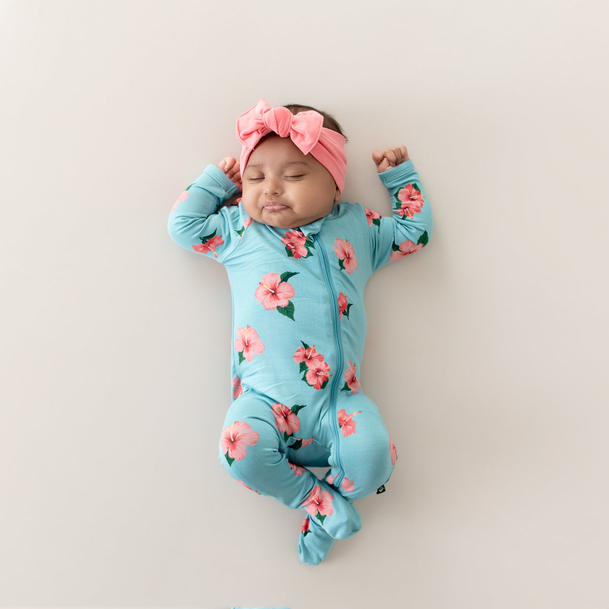 Baby wearing Zippered Footie in Hibiscus with matching pink bow headband