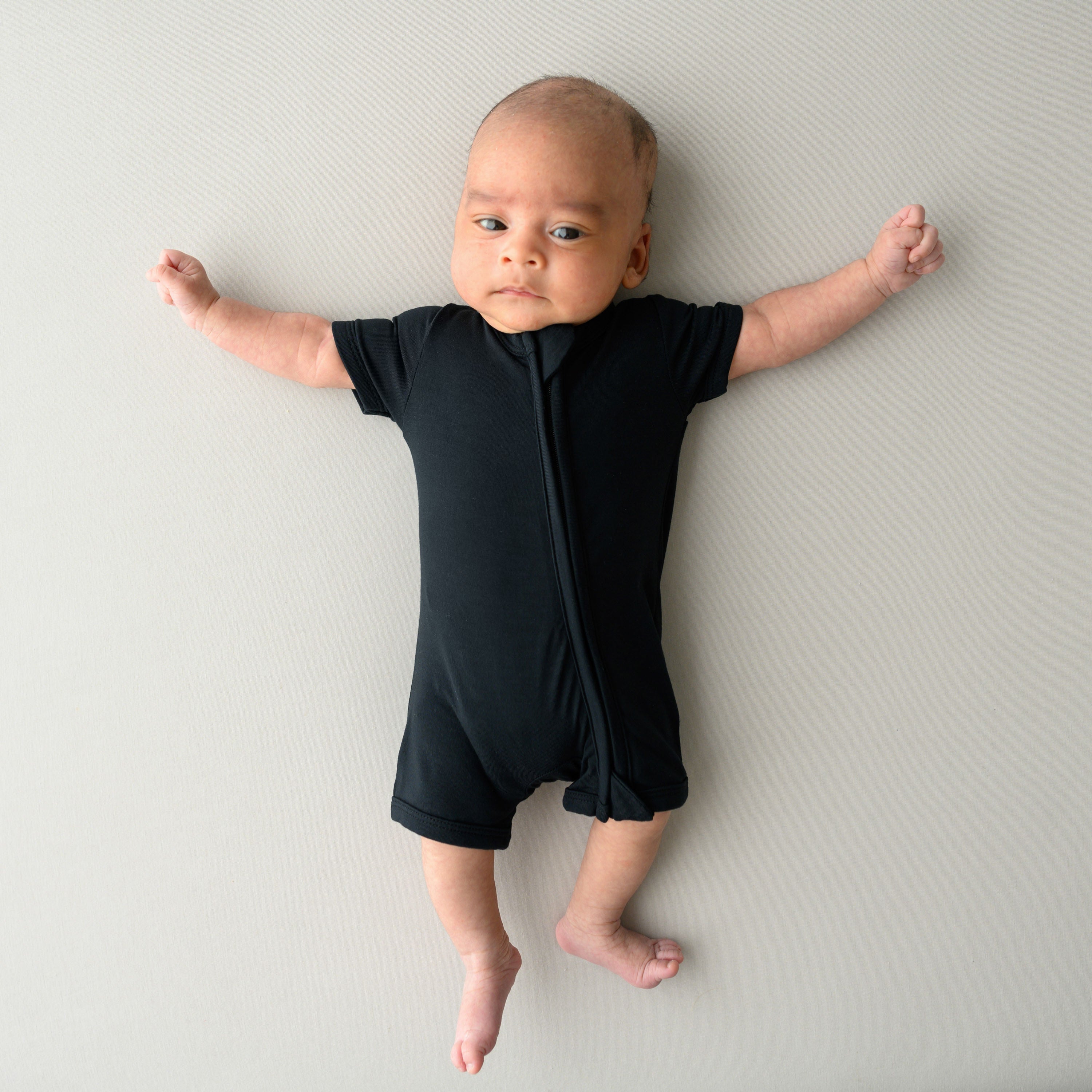 Infant wearing Kyte Baby Zippered Shortall Romper with dual zipper in Midnight