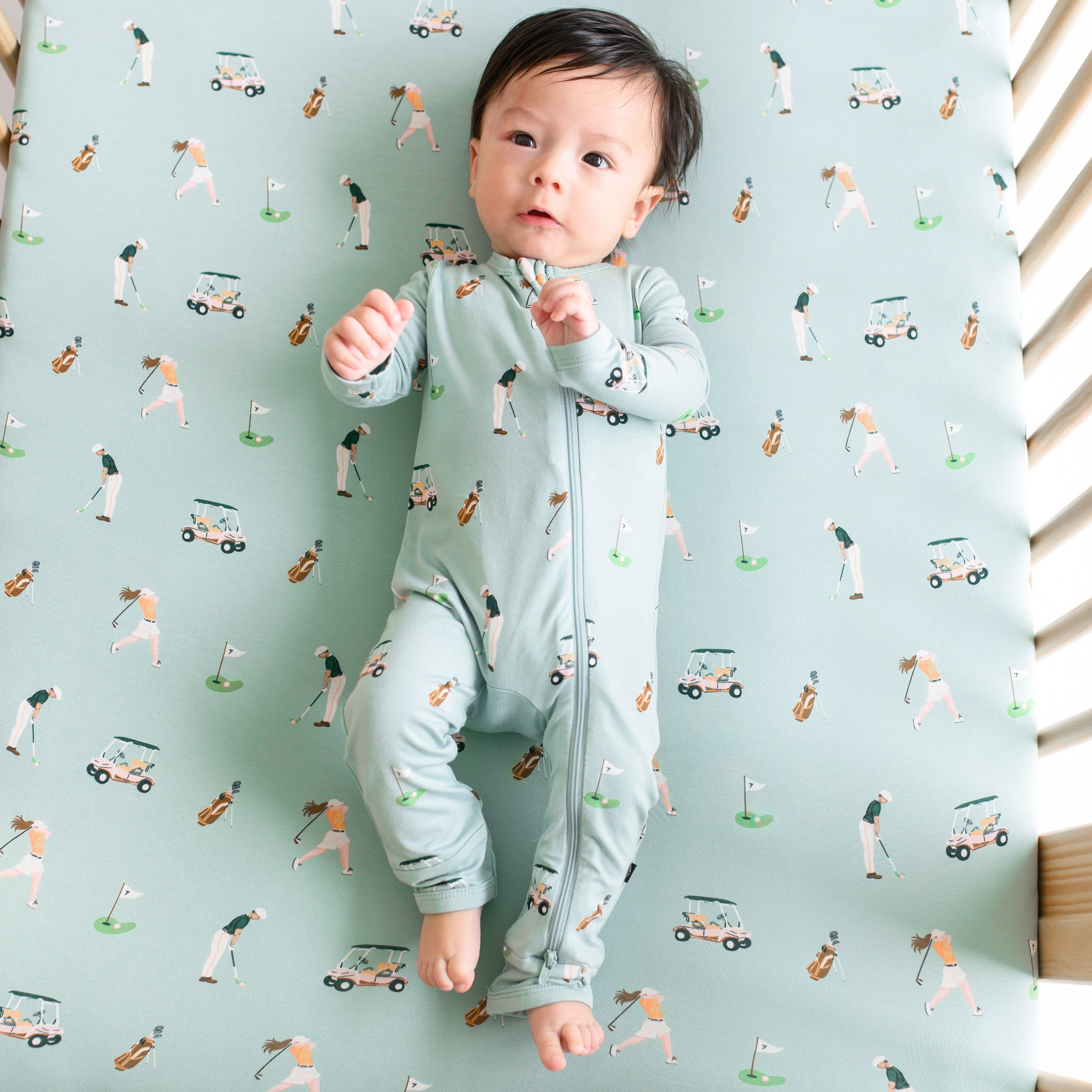 Infant wearing Zippered Romper pajamas laying on Golf Crib Sheet