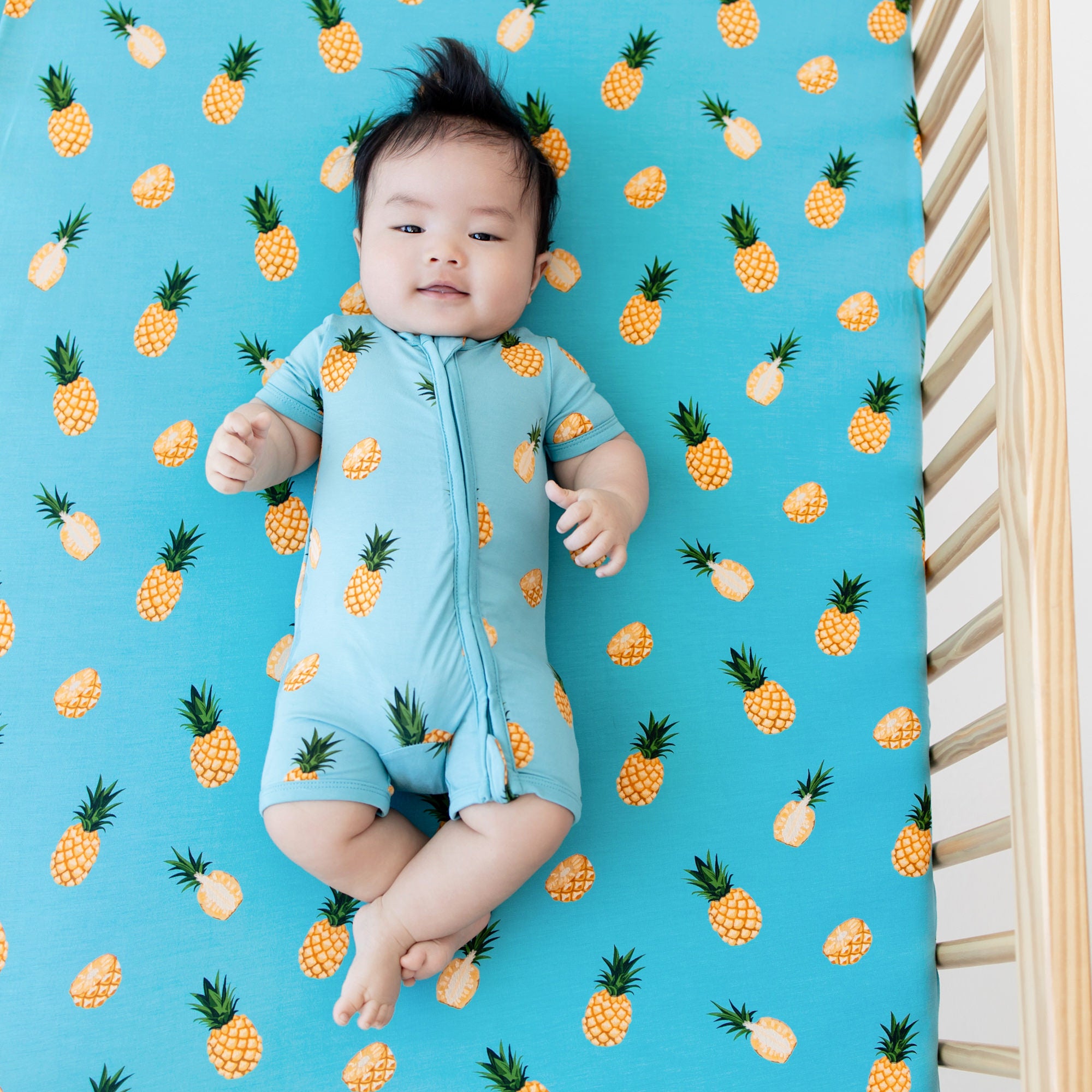 Crib Sheet in Pineapple on crib mattress with baby model wearing Pineapple Zippered Shortall