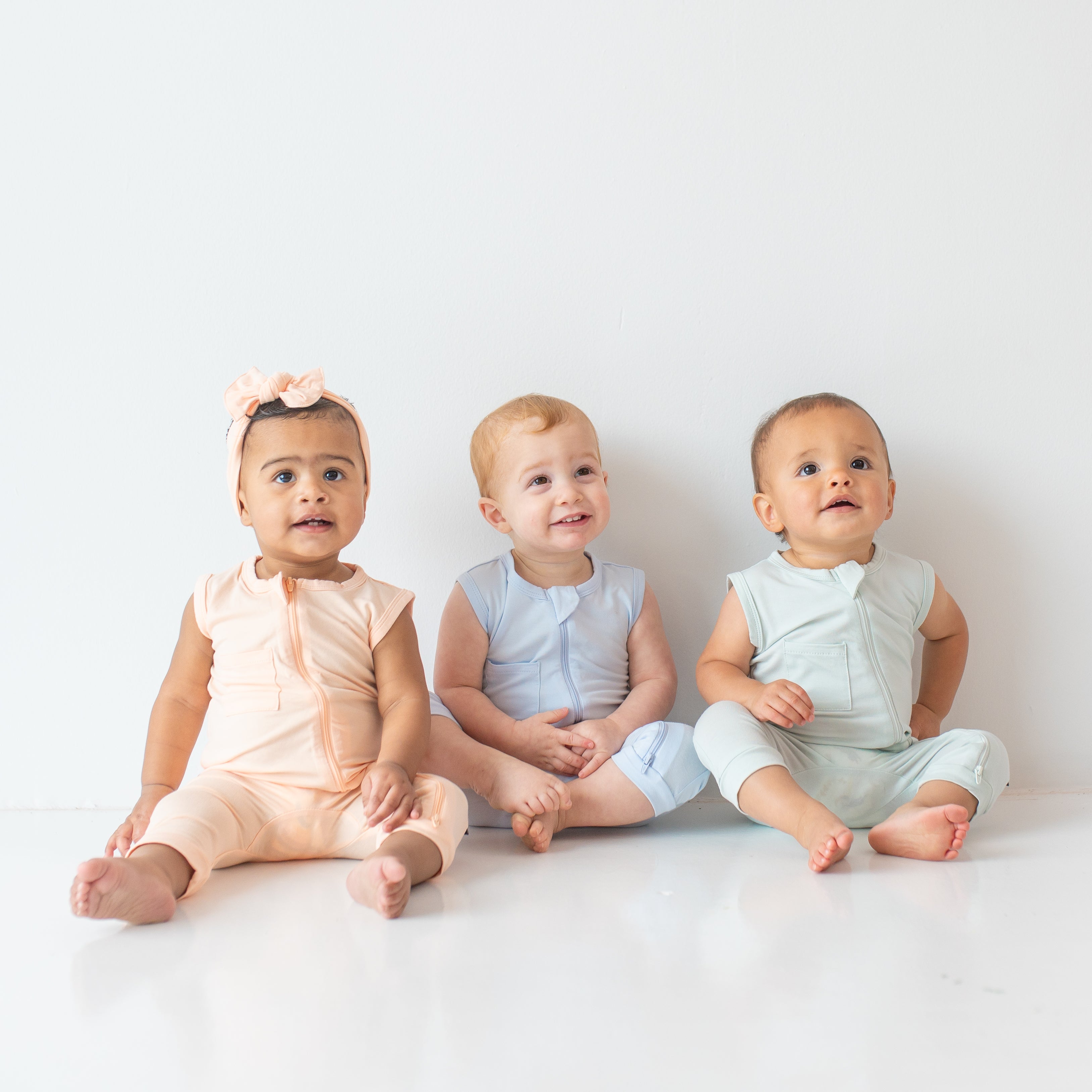 Three infants wearing the Zippered Sleeveless Romper in the Summer Solid colors