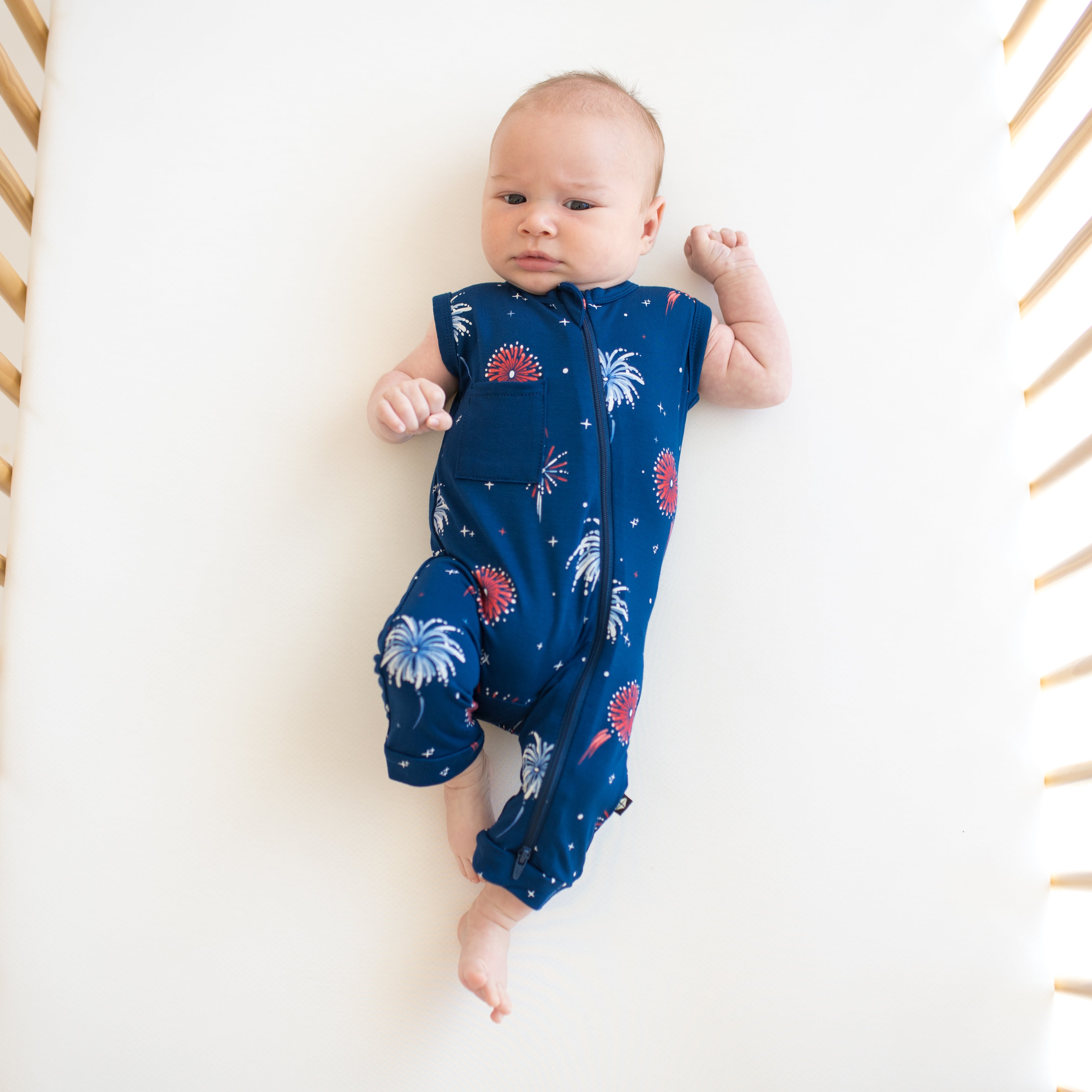 Baby wearing Zippered Sleeveless Romper in Celebration in a crib