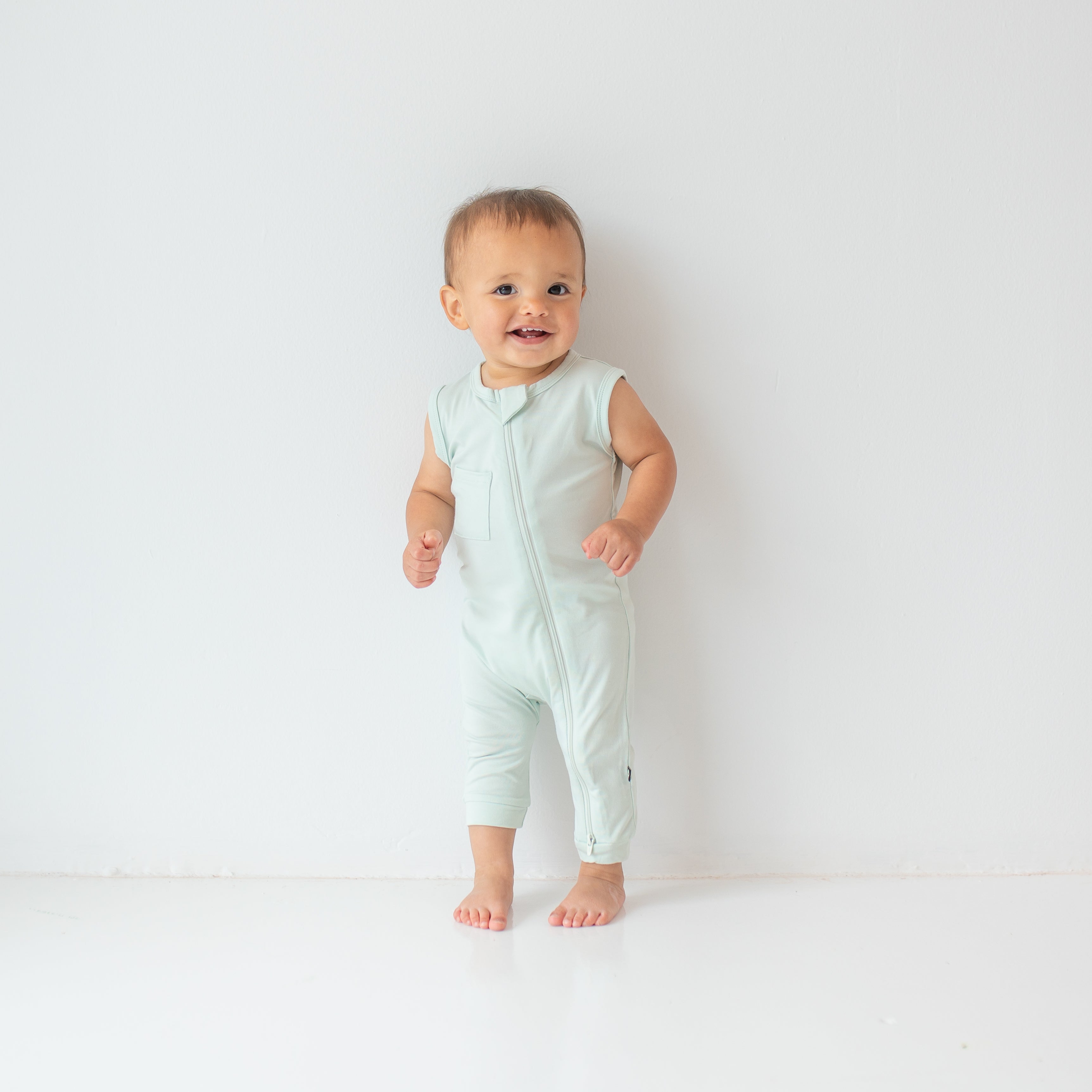 Smiling toddler wearing the Zippered Sleeveless Romper in Dew