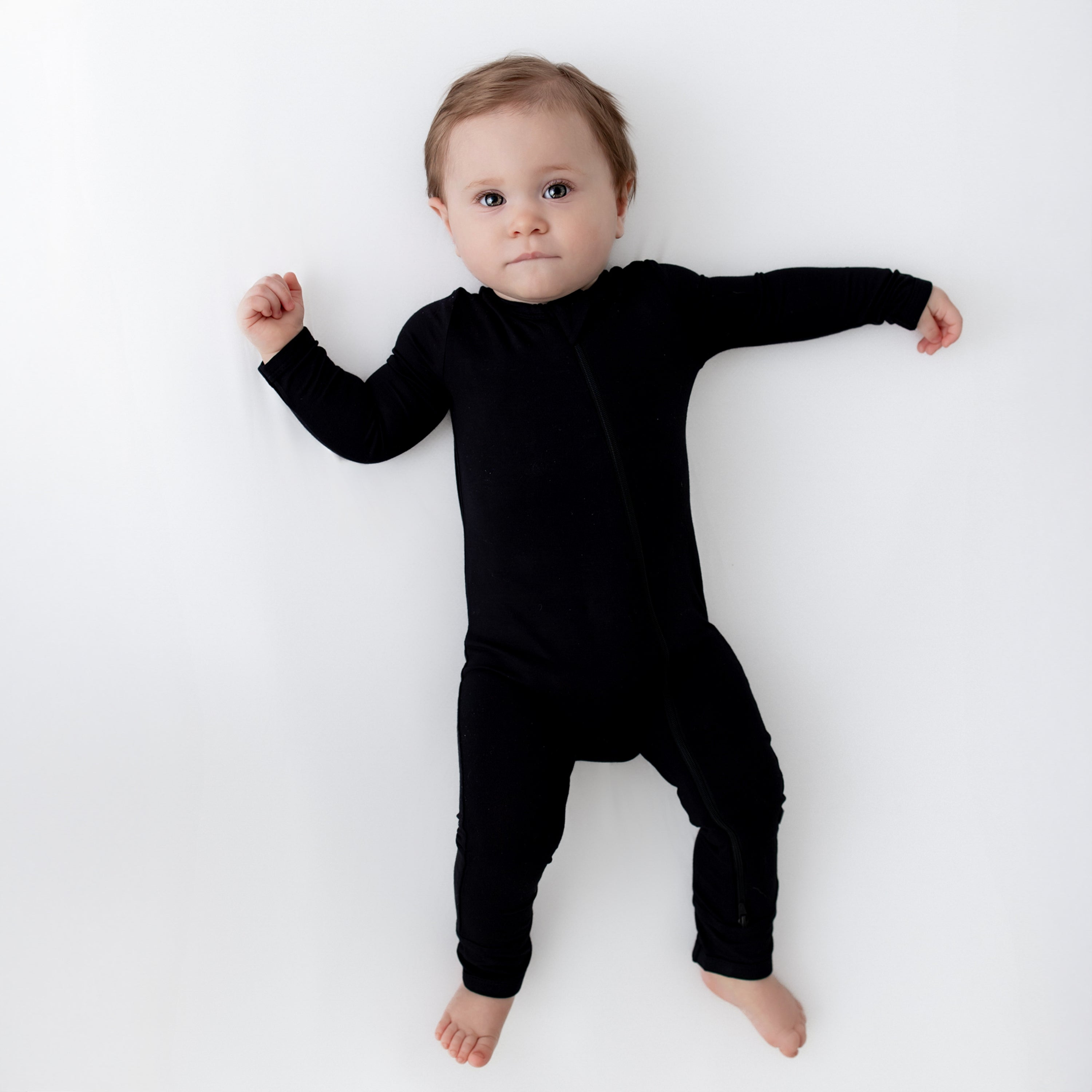 Baby laying on a white surface and wearing Zippered Romper in Midnight