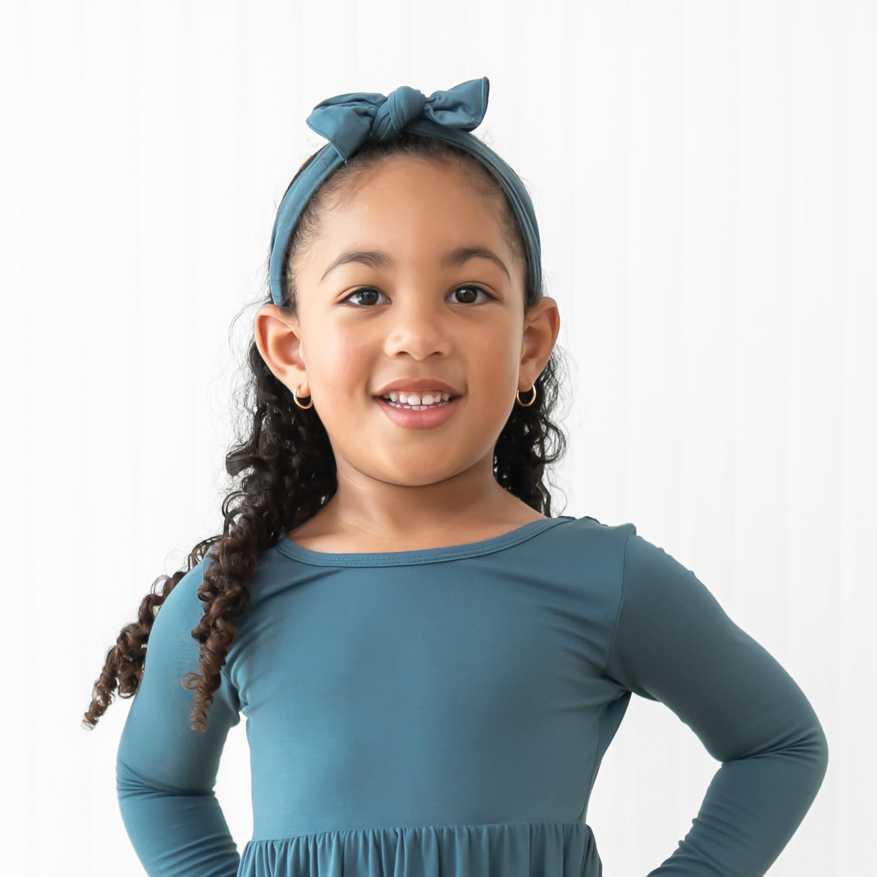Smiling girl wearing the Knotted Bow Headband in Atlantic paired with a matching long sleeve twirl dress