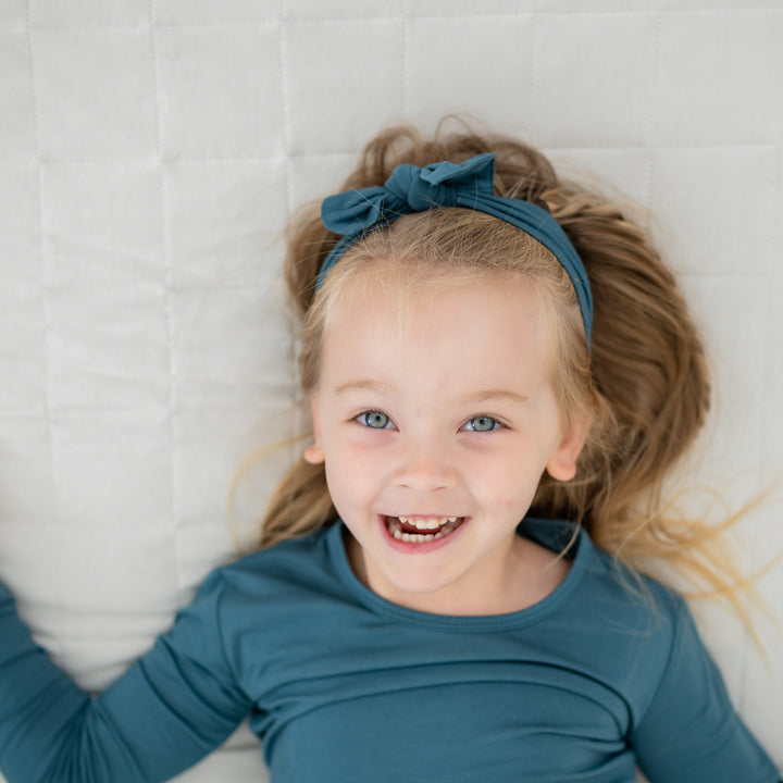 Smiling girl laying on a blanket wearing the Knotted Bow Headband in Atlantic