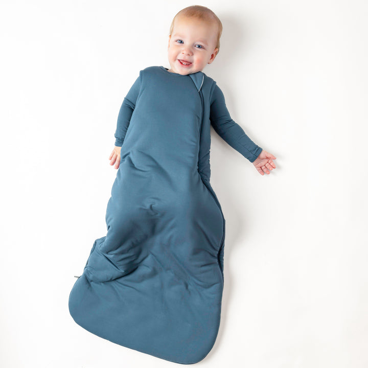 Infant laying down wearing the Sleep Bag in Atlantic 2.5 wearing a matching romper underneath