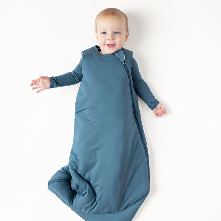 Smiling infant wearing the Sleep Bag in Atlantic 2.5 with a matching long sleeve romper on underneath