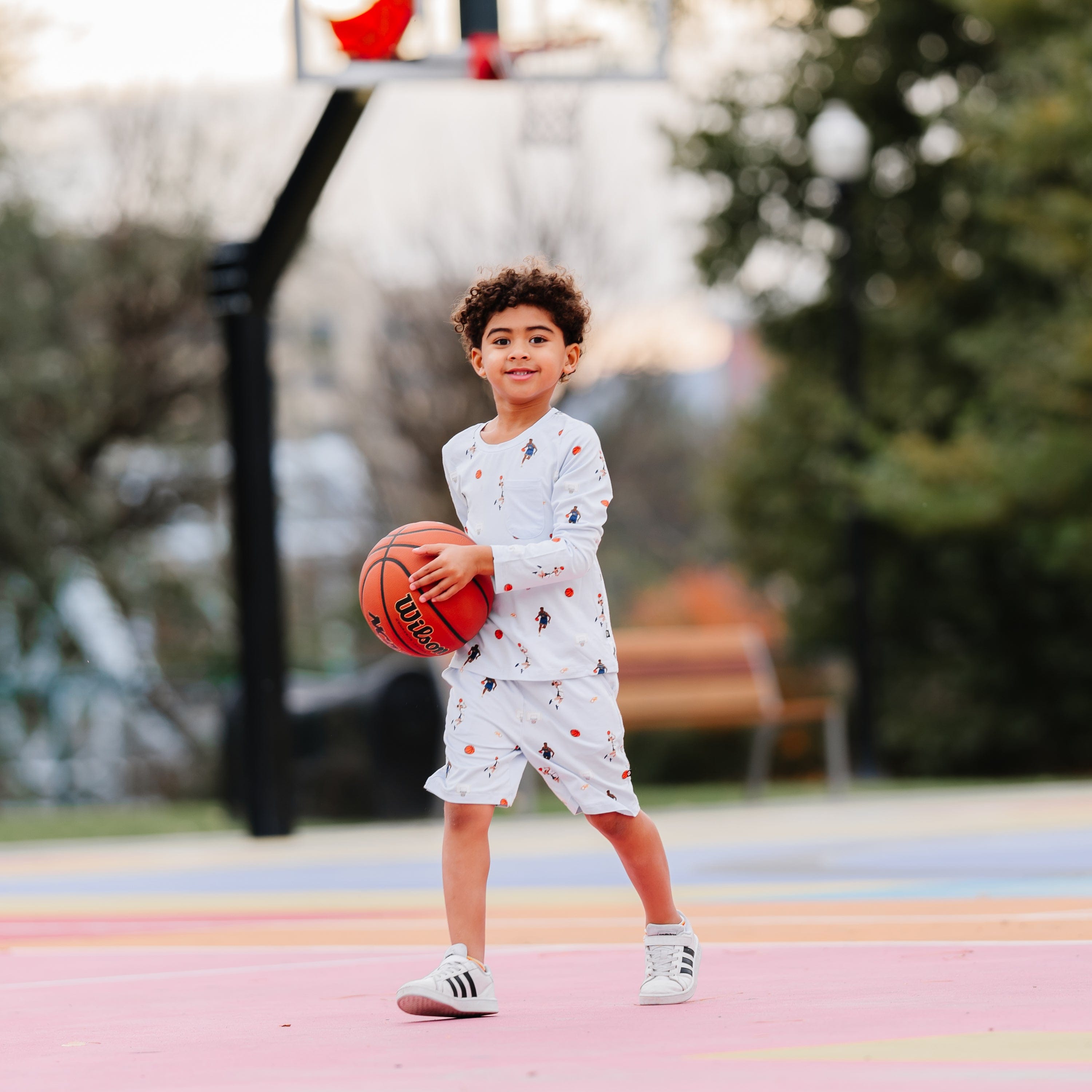 Young boy walking on a basketball court holding a basketball wearing the Long Sleeve Toddler Crew Neck Tee in Basketball and matching drawstring shorts